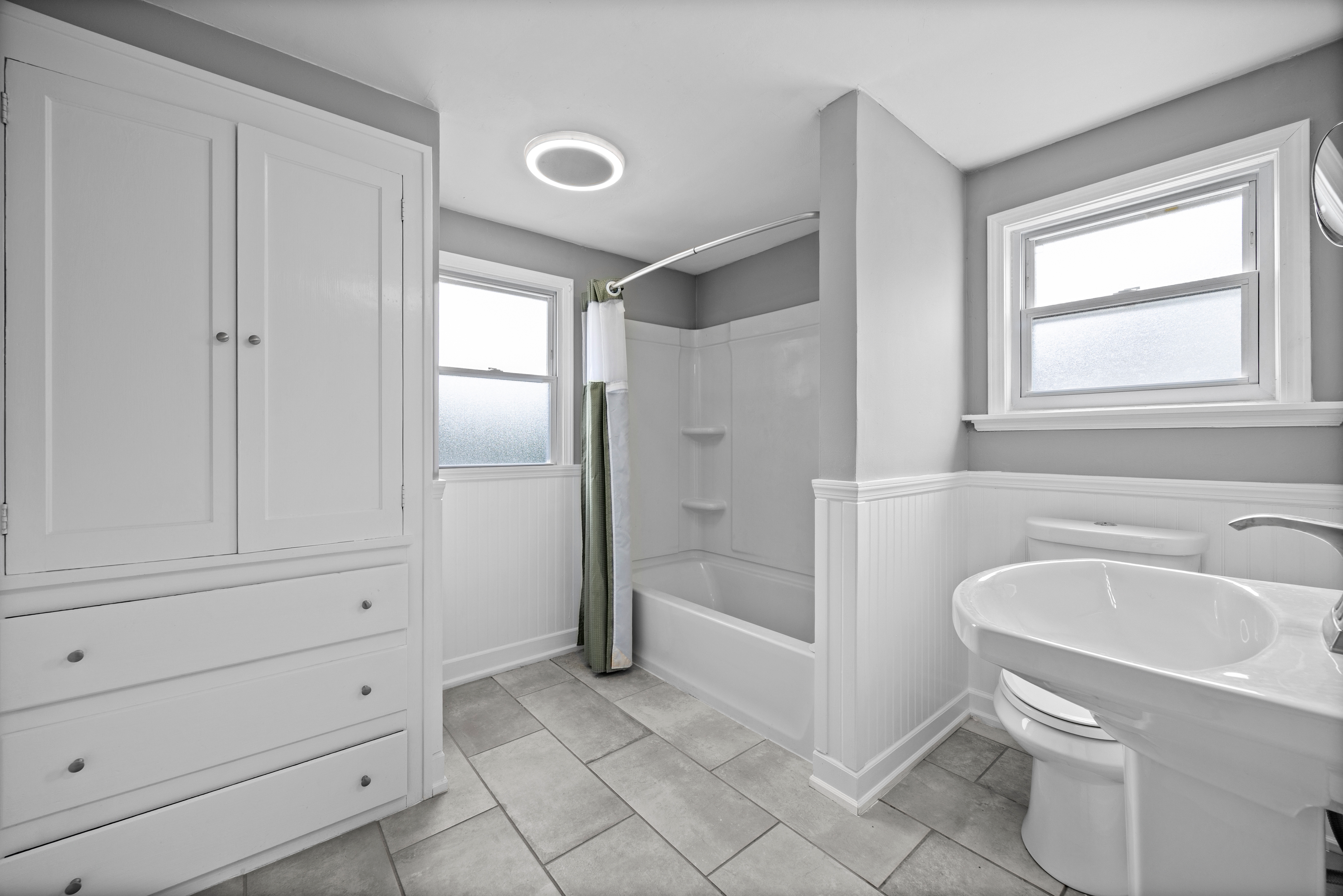 Full bathroom with pedestal sink, white built-in cabinetry, and plank-style tile flooring