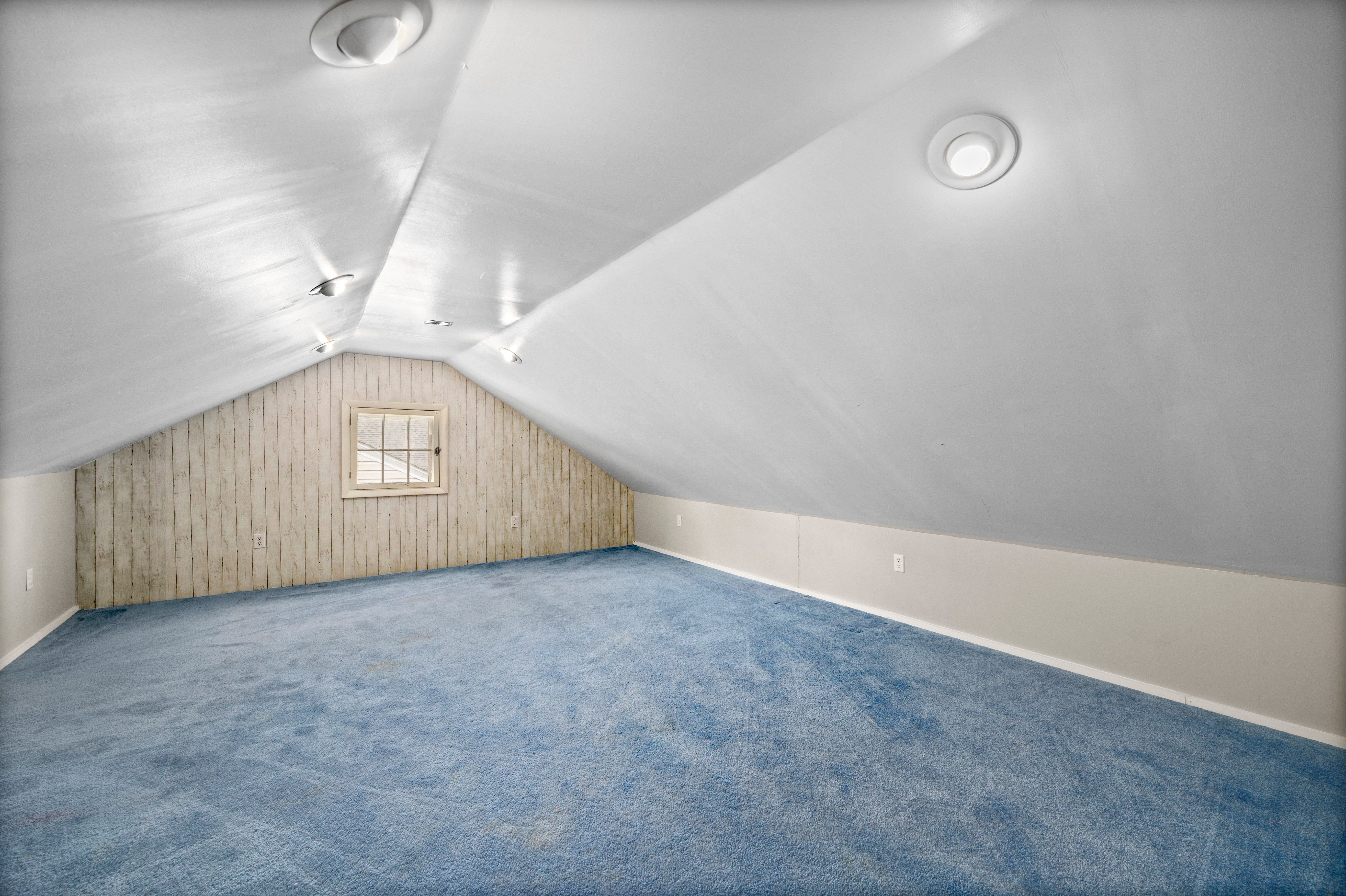 Upper-level bedroom with vaulted ceilings, wood-paneled accent wall, and blue carpeting