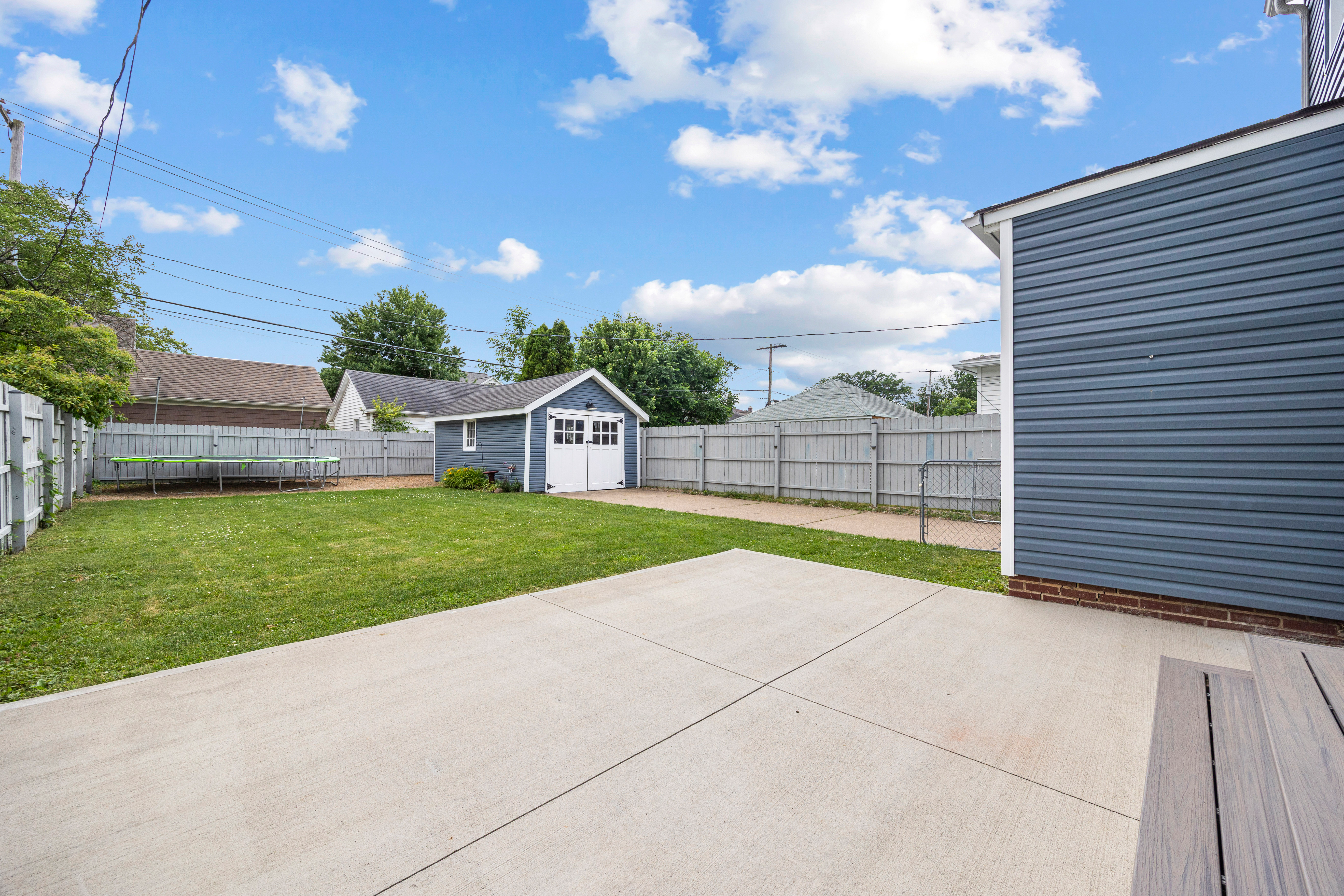 Backyard with concrete patio, fenced lawn, and detached garage under blue sky