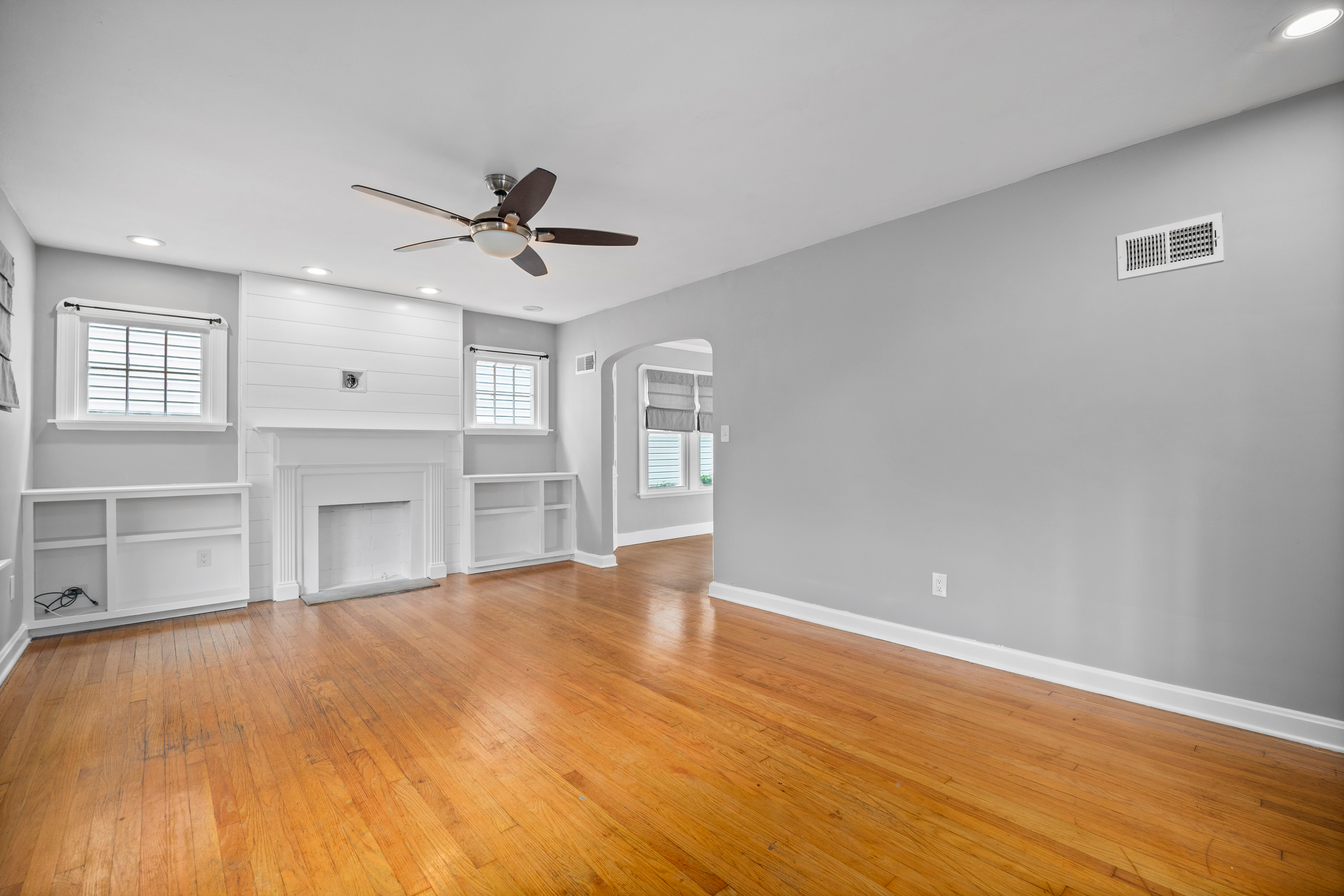 Living room with hardwood floors, white shiplap fireplace mantle, and built-in shelving