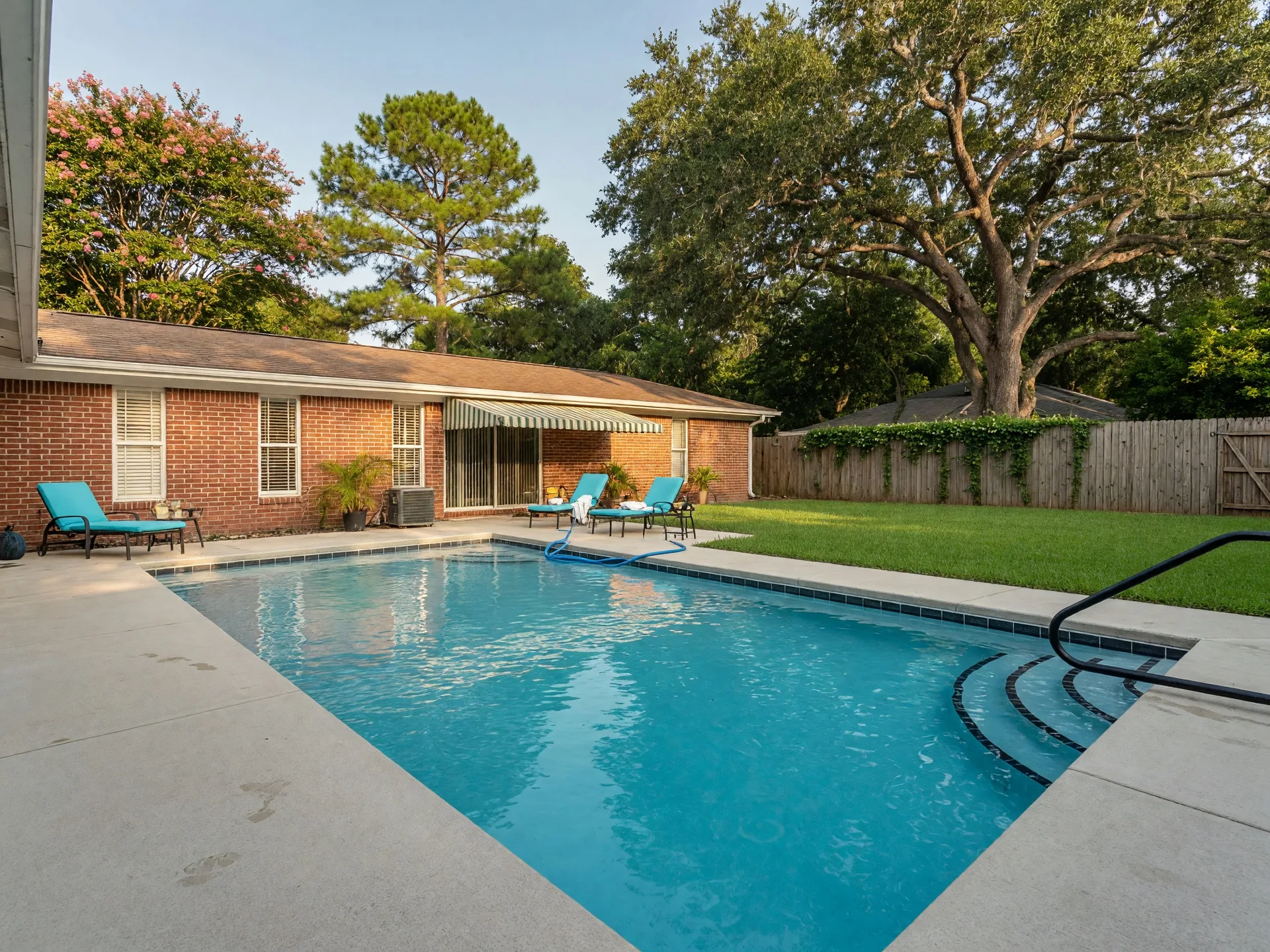 Private backyard swimming pool at a single-story brick home in Houston, Texas, with clear blue water and spacious patio surrounded by mature trees