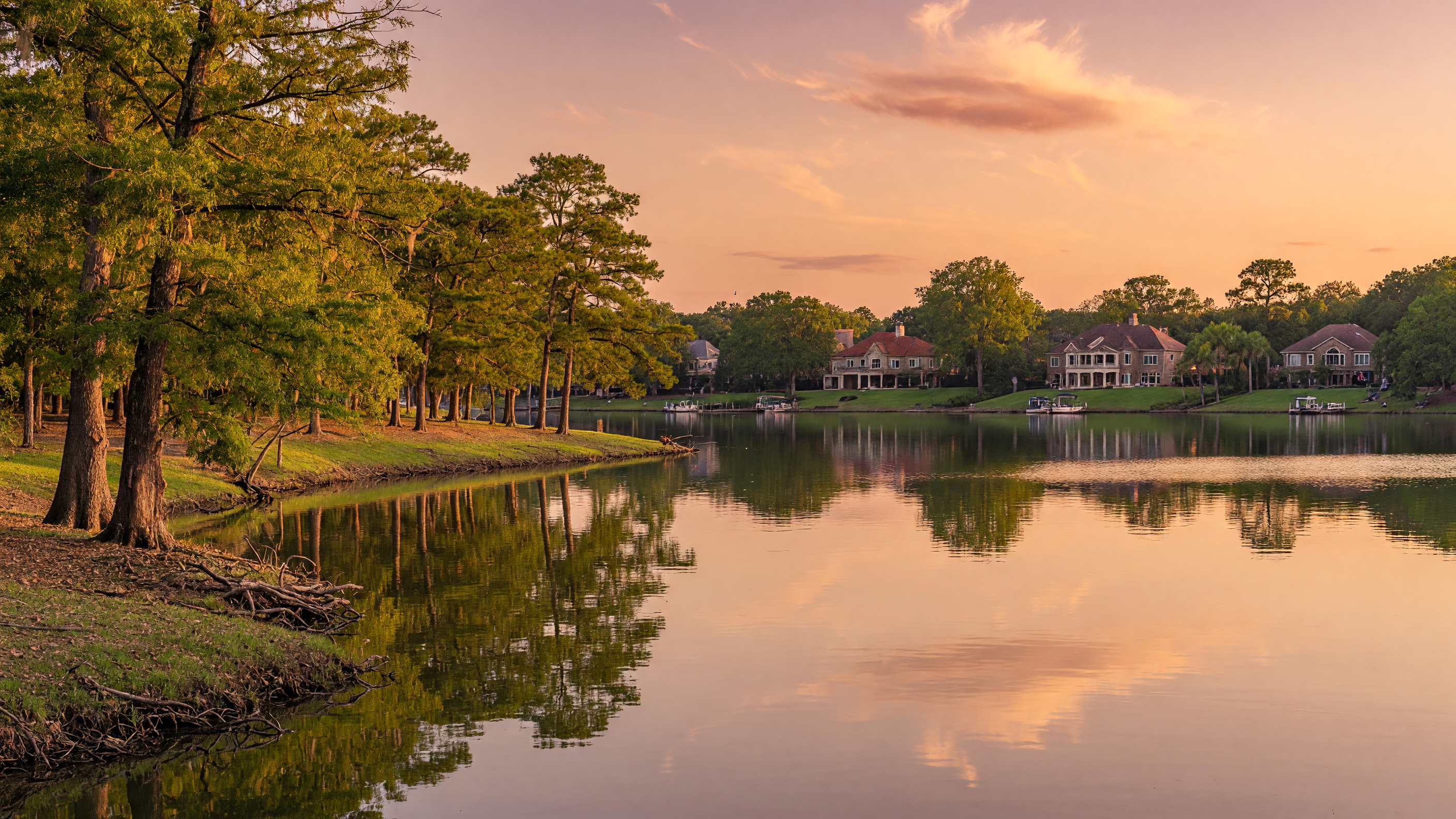 A peaceful Lake Houston shoreline at golden hour with mature trees and suburban homes in the distance, representing the lifestyle buyers can expect in the Lake Houston area
