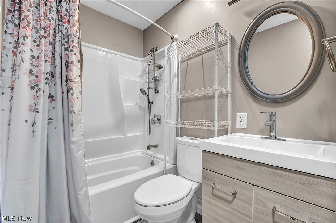 Updated full bathroom with light wood vanity, white tub surround, and round framed mirror