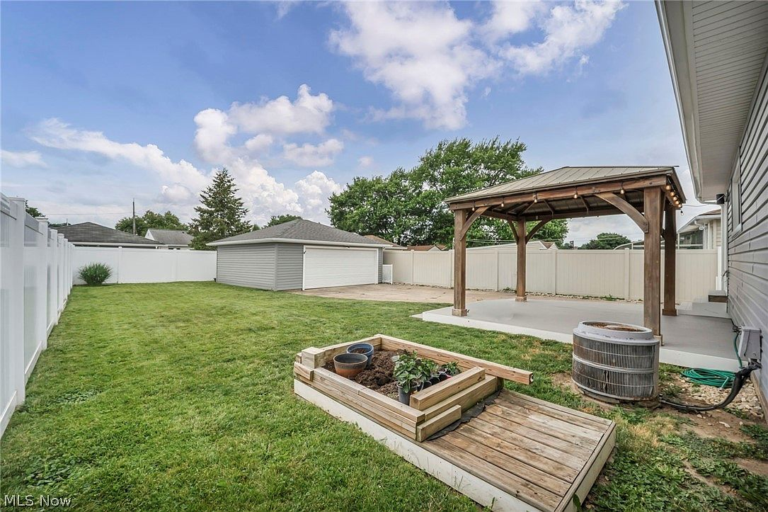 Fully fenced backyard with detached garage, wood pergola, and garden beds