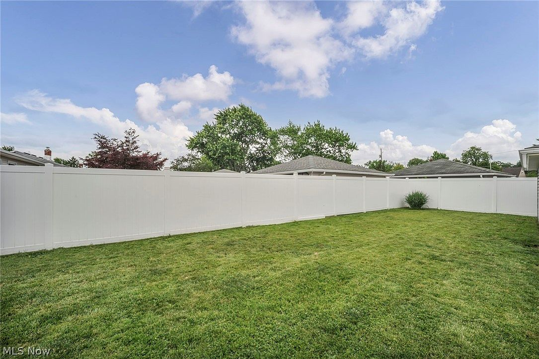 Spacious fenced backyard with large grassy lawn and white vinyl fencing