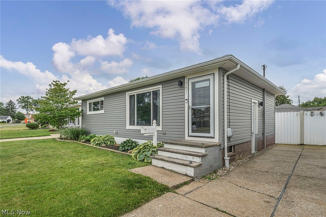 Street-level view of the ranch home with concrete driveway and white privacy fencing
