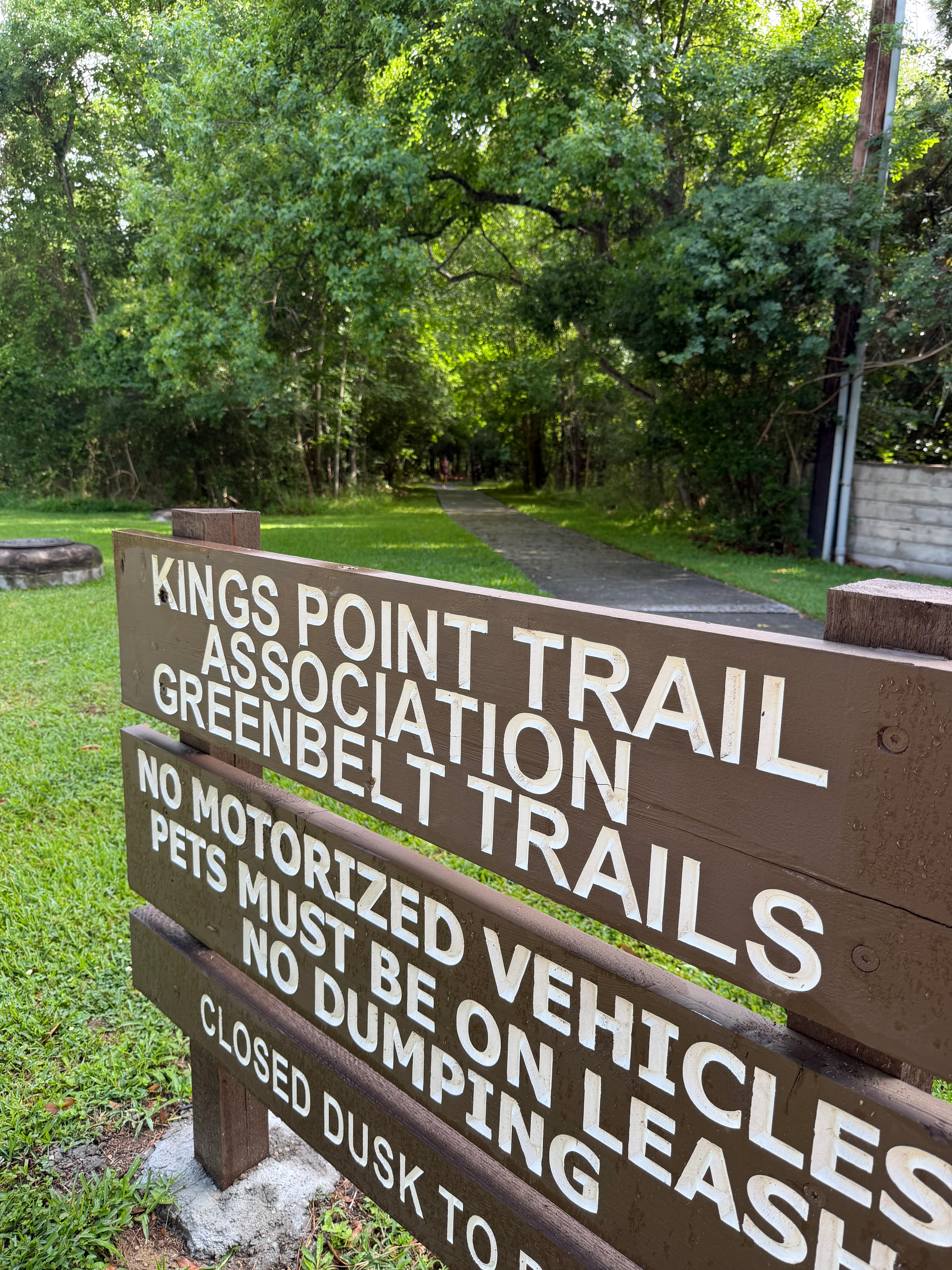 Kings Point Trail Association sign with walking path and trees in the background