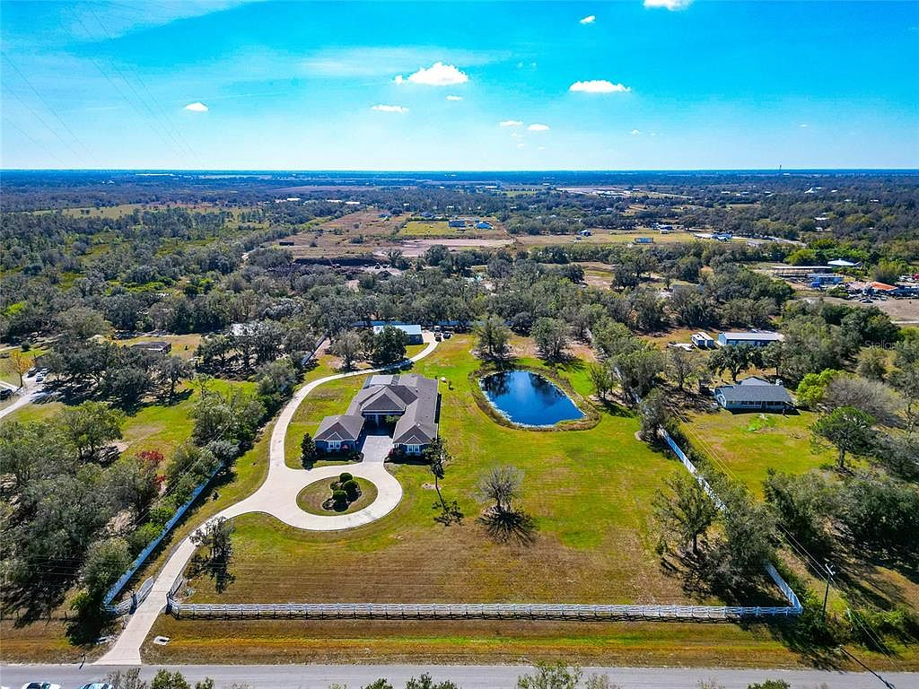 High-altitude aerial view showing all three buildings, driveway and pond on the five-acre estate