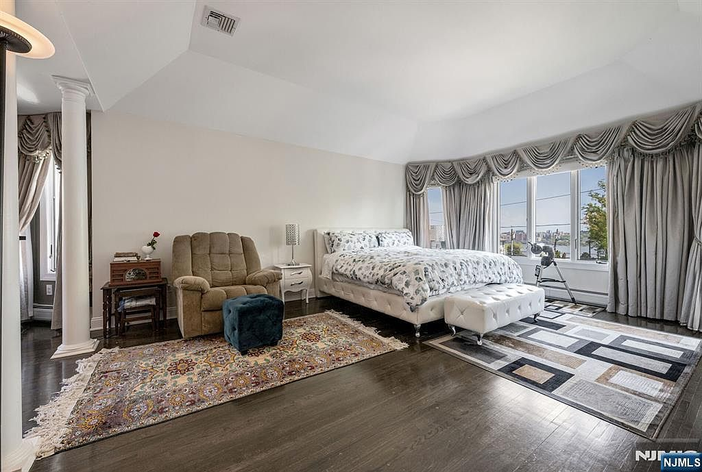 Primary suite with tray ceiling, NYC skyline view, and dark hardwood floors