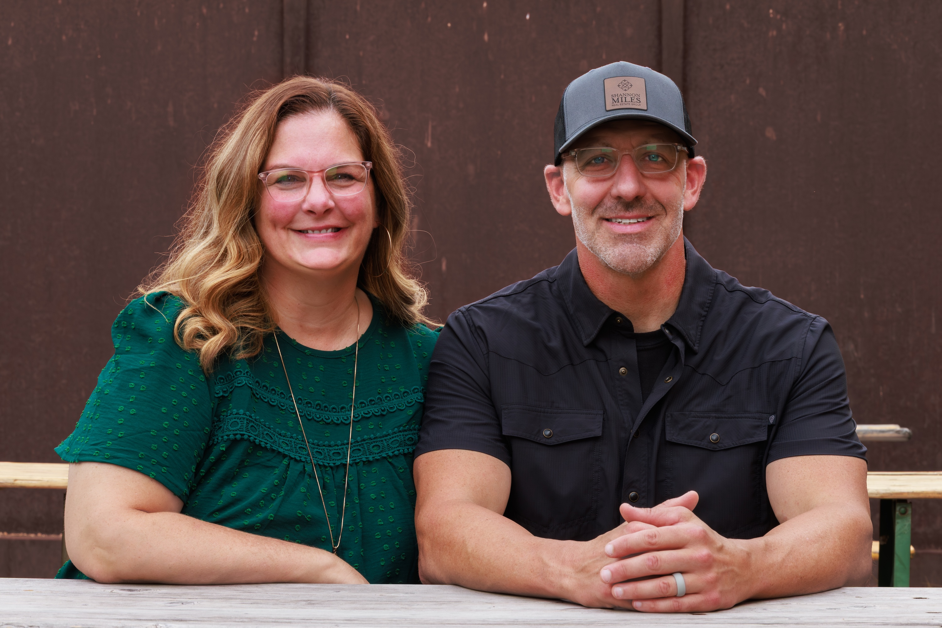 Shannon and Scott Miles smiling together at a wooden table inside their Paris, Texas office