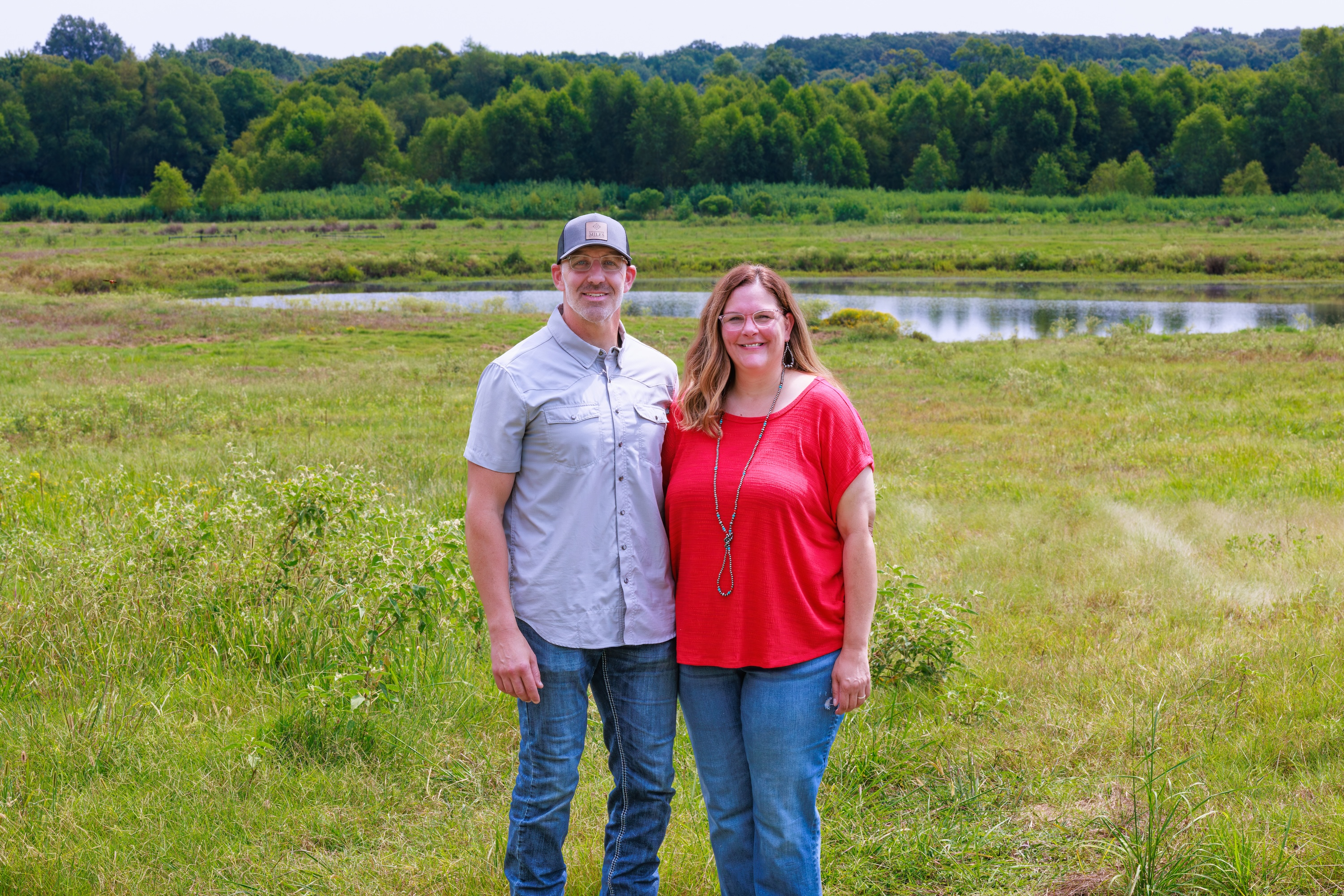 Shannon and Scott Miles standing together in a field with a pond and trees in Northeast Texas