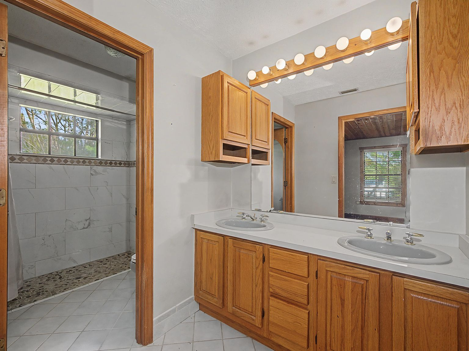 Primary bathroom with oak dual vanity and globe-bulb light bar
