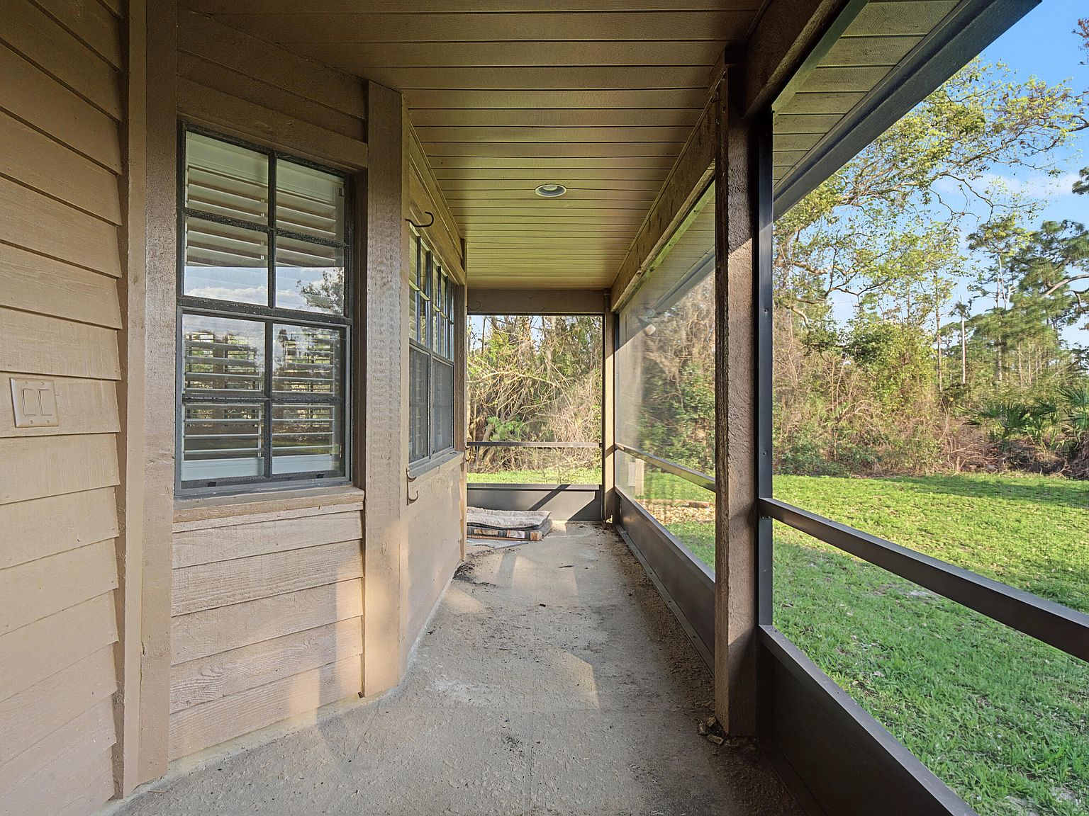 Screened back porch with concrete flooring and wood-paneled walls