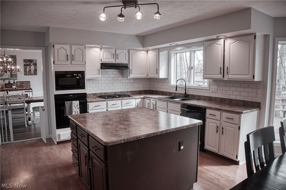 Kitchen with white shaker cabinets, dark granite countertops, subway tile backsplash, and center island