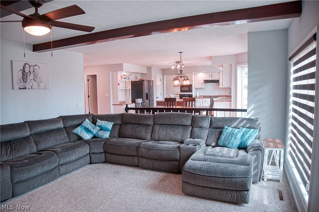 Open-plan living room flowing into dining area and kitchen with dark wood beam ceiling