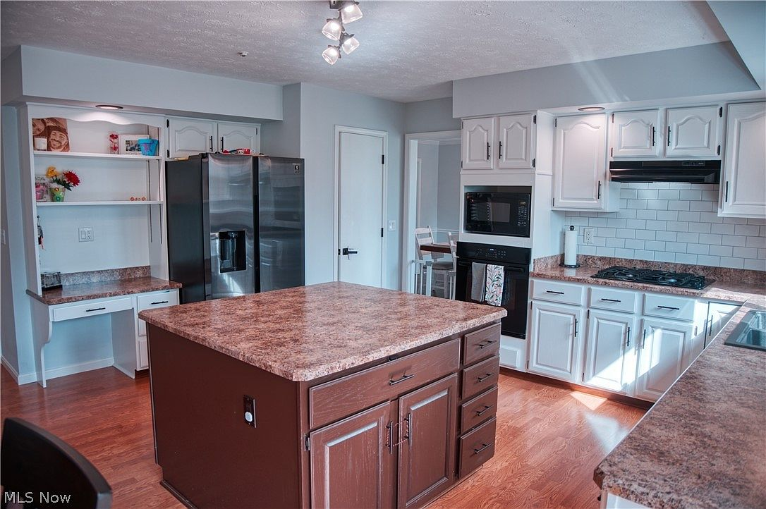 Kitchen showing white cabinetry, dark stained oak island, and subway tile backsplash