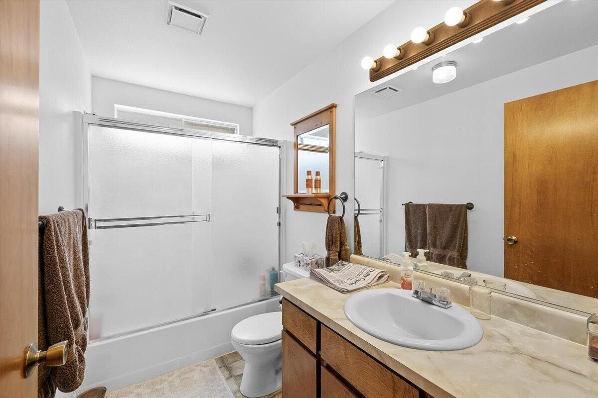 Bathroom with oak vanity, stone-look countertop, and shower-tub combo