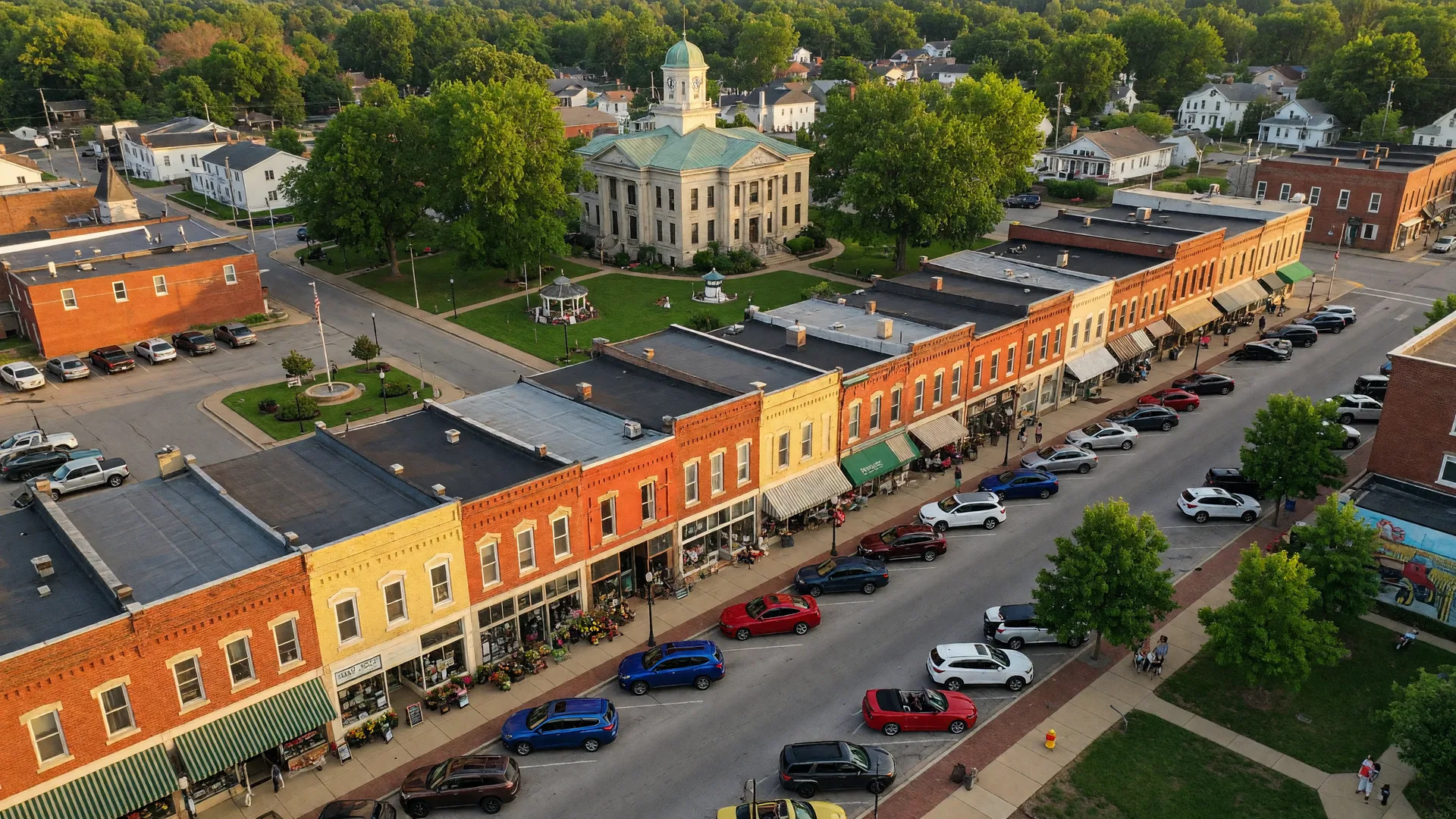 Aerial view of a charming Ohio small town downtown with historic brick storefronts, tree-lined streets, and a courthouse square on a warm summer afternoon