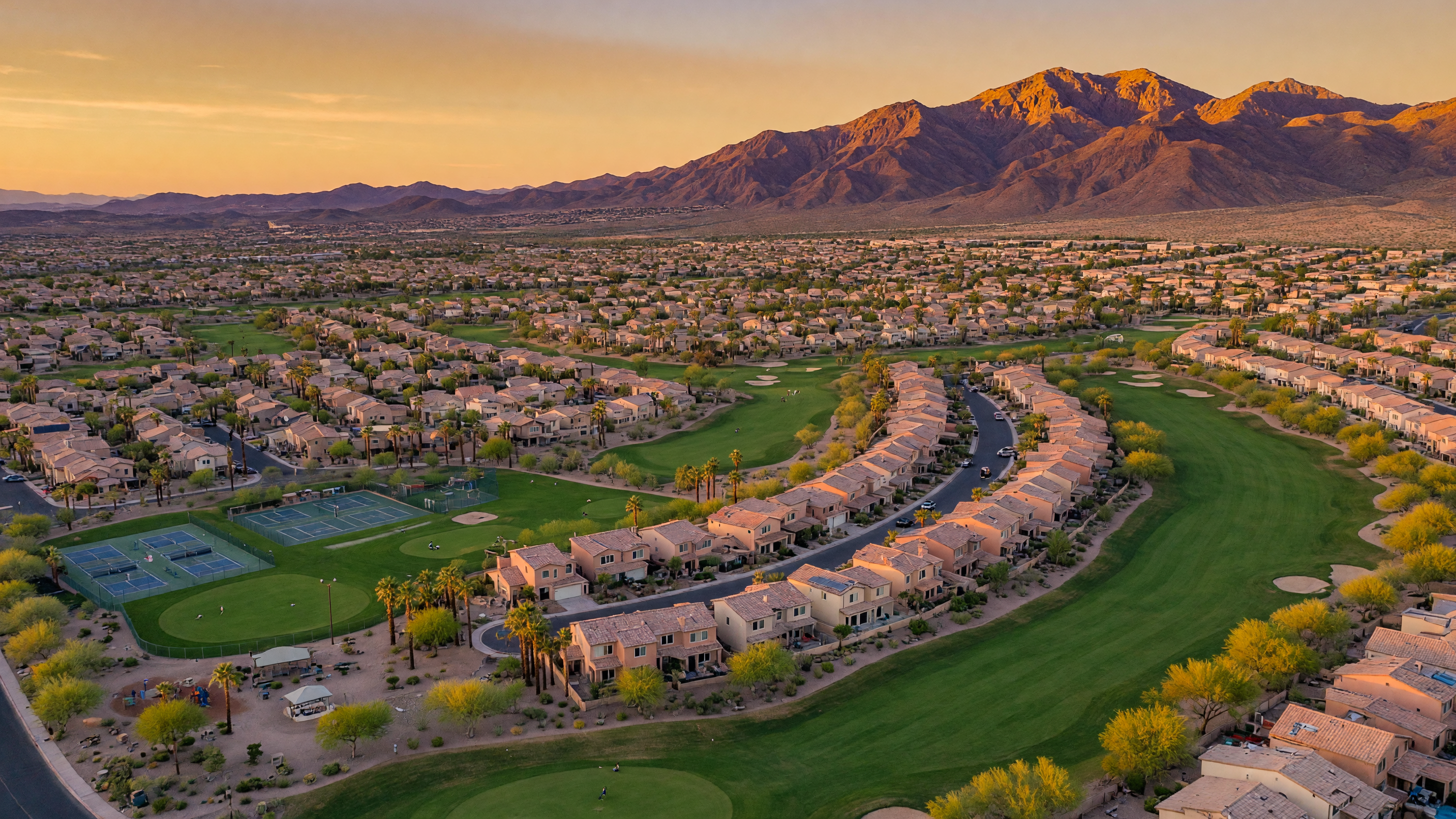 Aerial view of the Southern Highlands master-planned community in Southwest Las Vegas showing homes, golf course fairways, parks, and the Spring Mountains at golden hour