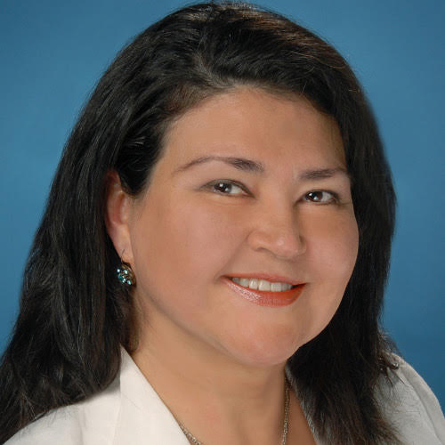 Matilde (Mati), professional headshot in a white blazer against a blue backdrop