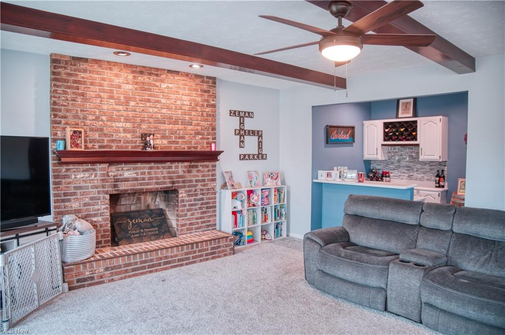 Living room featuring red brick fireplace with wood mantel and exposed ceiling beams