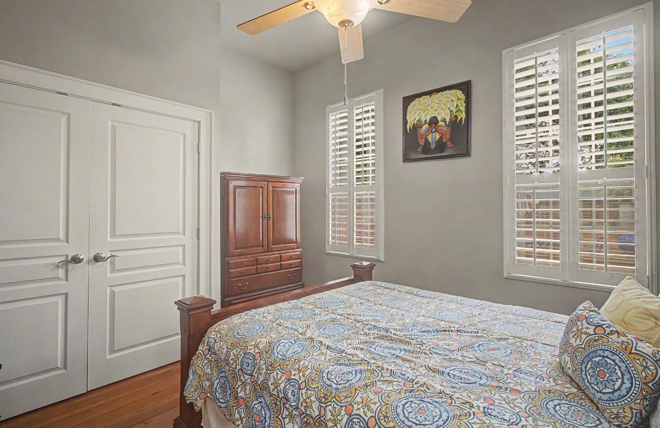 Second bedroom with heart pine wood floors, light grey walls, and plantation shutters