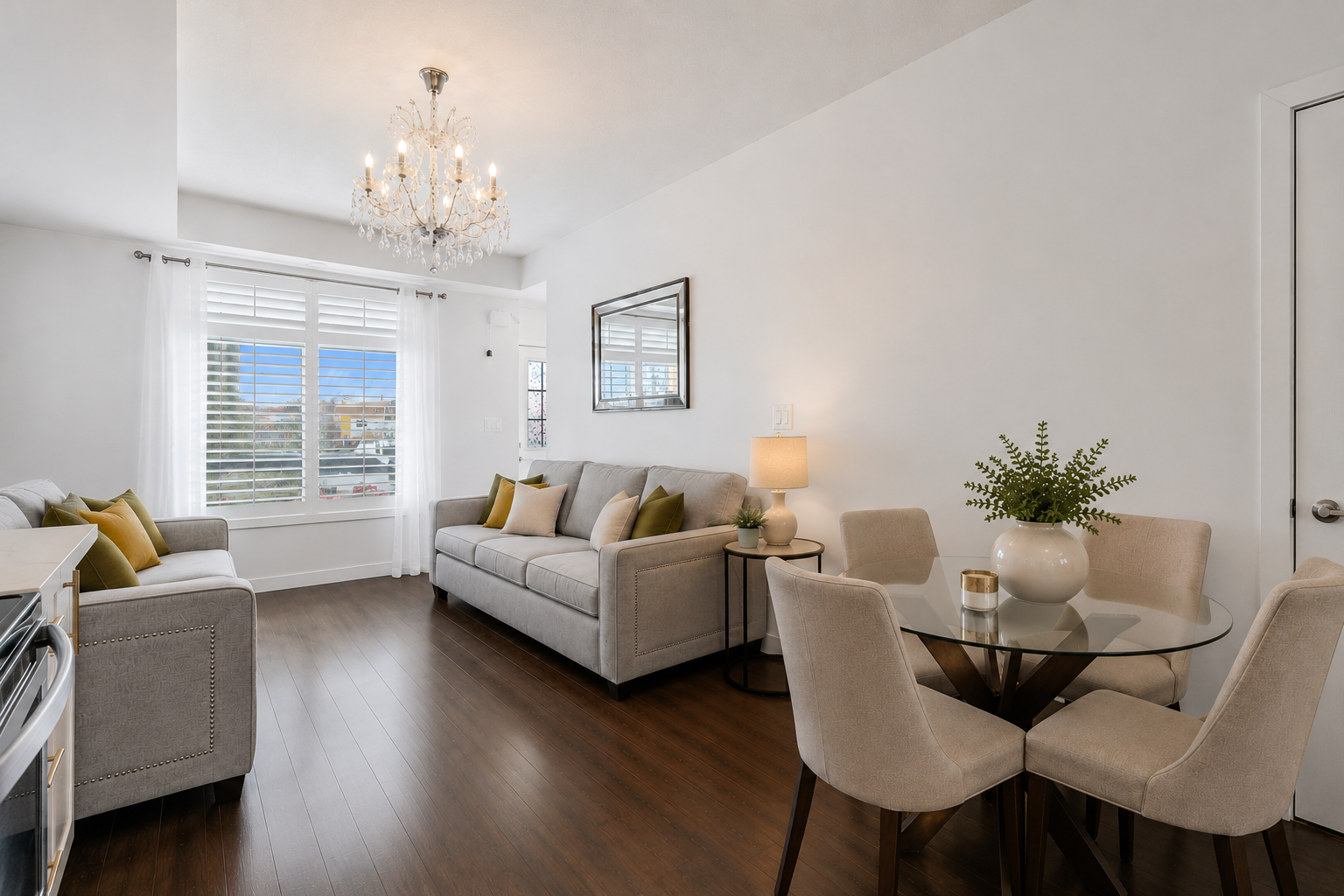 Open-concept living and dining area with sofa, loveseat, glass-top dining table, and natural light — virtually staged