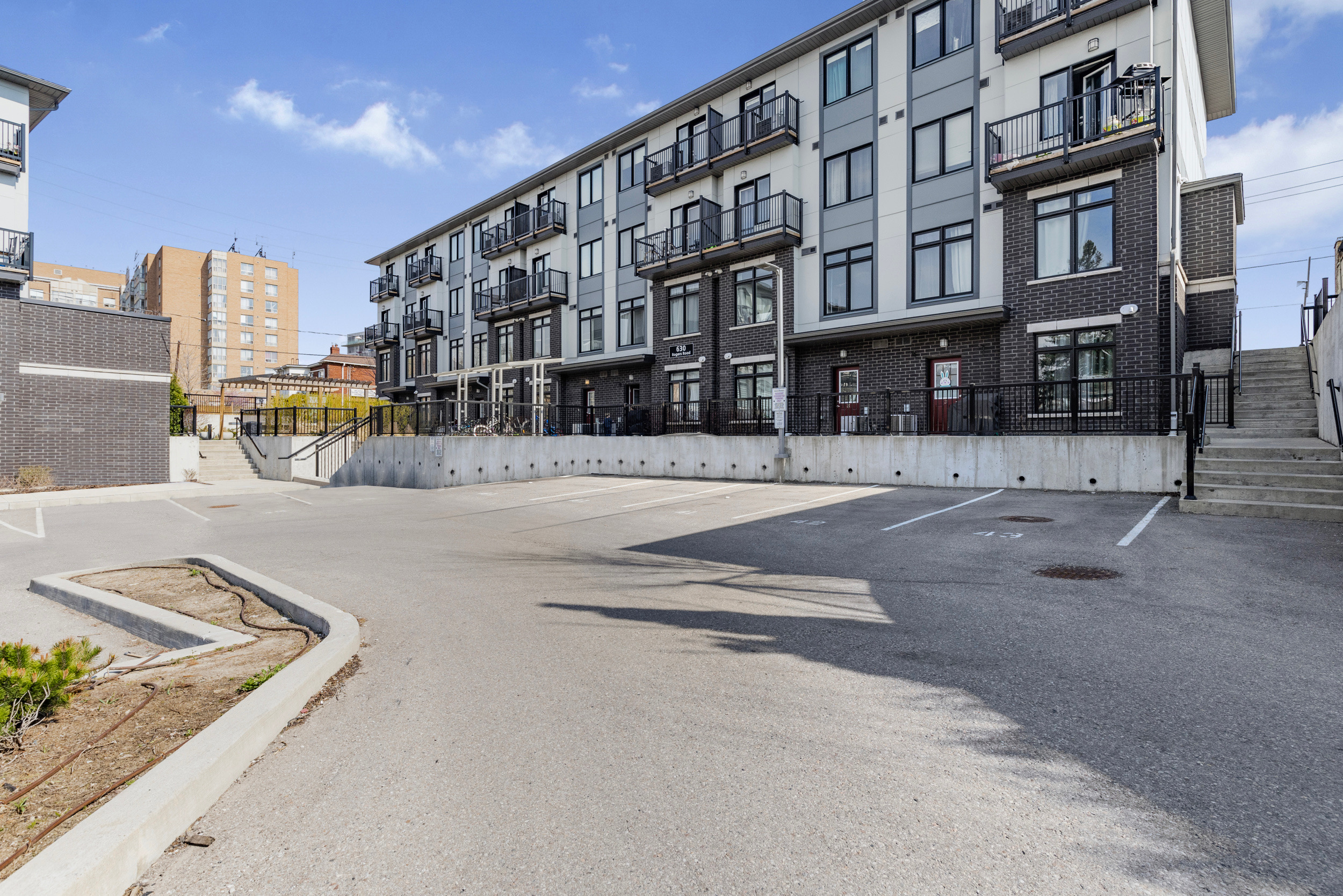 Street-level view of the multi-unit townhouse complex with grey and white paneled siding, balconies, and concrete stairs