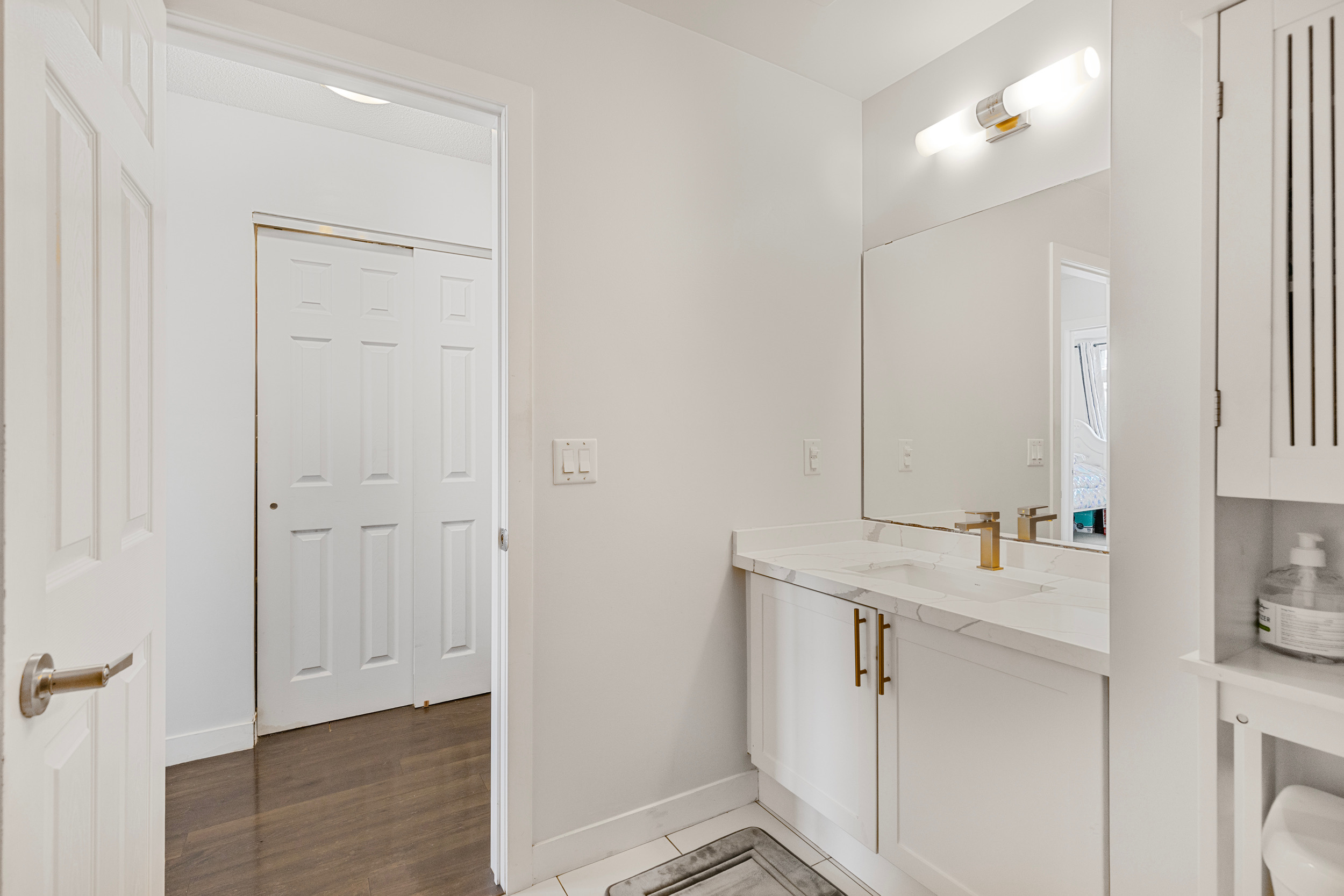 Bathroom vanity detail with marble-top counter, gold faucet, wall light fixture, and mirror