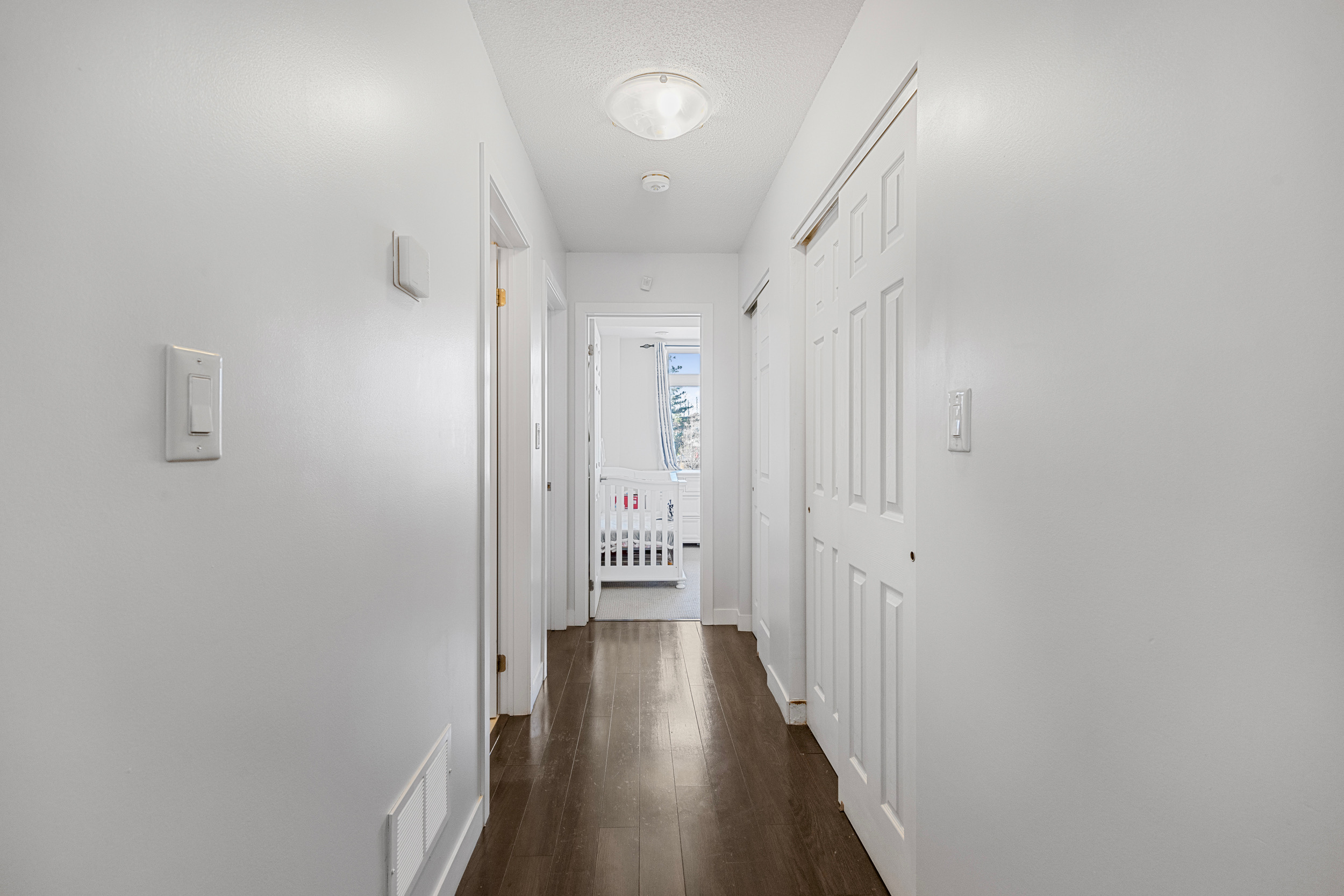 Interior hallway with crisp white walls, dark-stained laminate flooring, and paneled closet doors