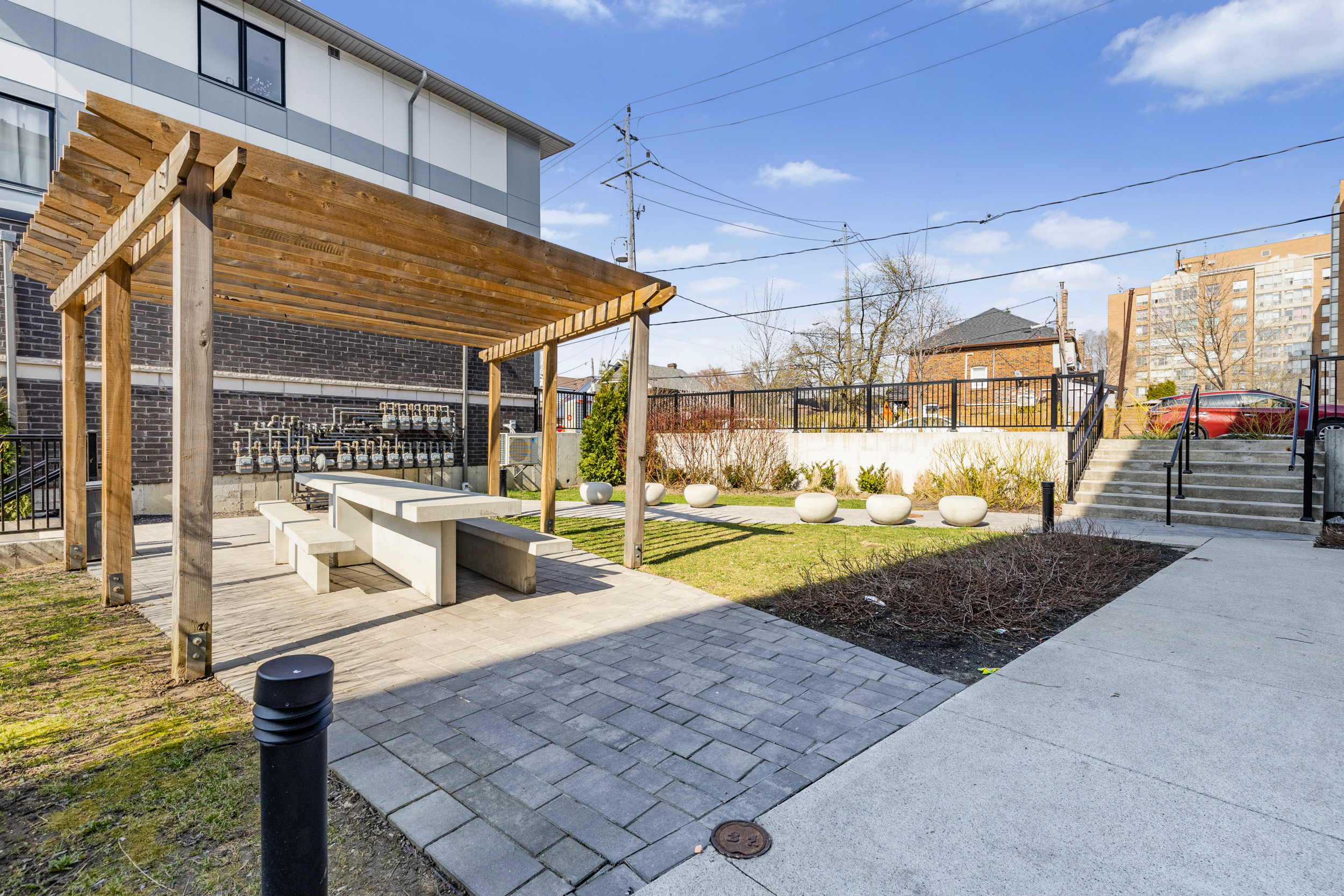 Common area patio with wooden pergola, concrete pavers, small lawn, and retaining wall