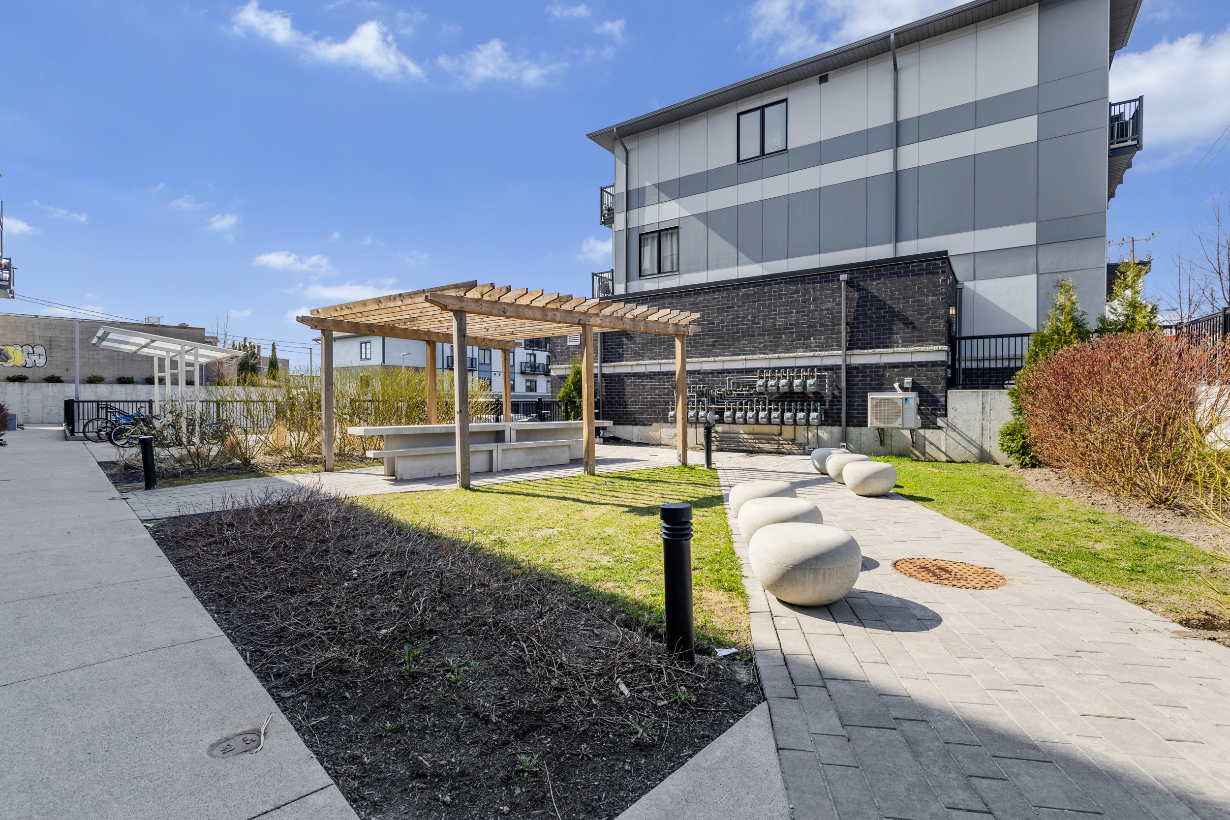 Community courtyard with pergola, concrete table, stone seating, paved walkway, and bike parking area