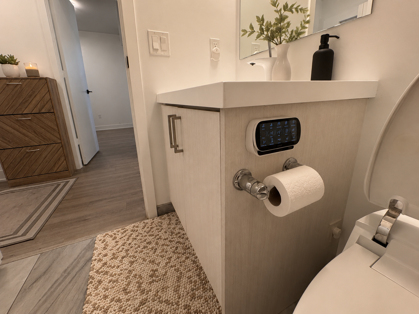 Main bathroom vanity with light wood-grain finish, smart home control panel, and chevron-patterned chest of drawers