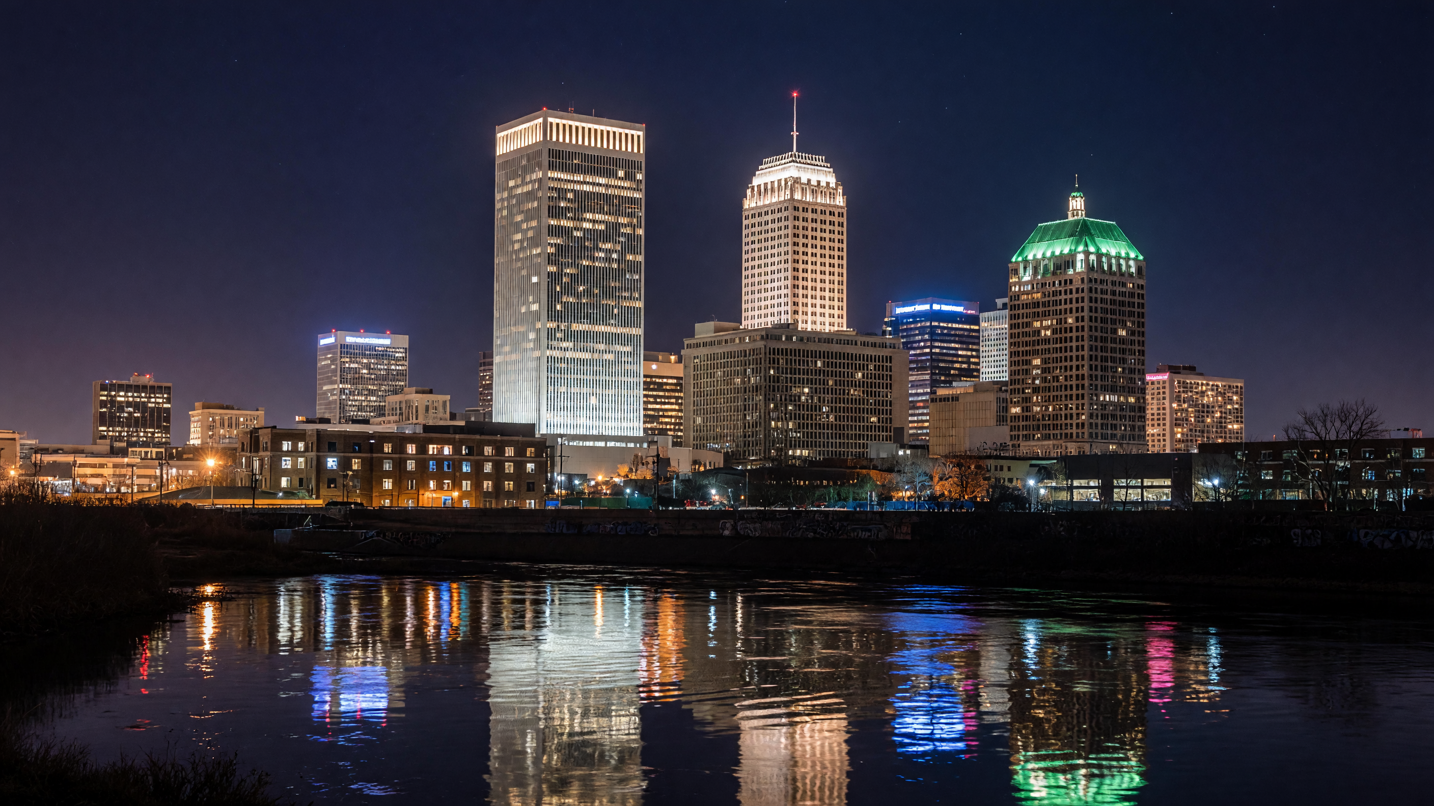 Downtown Tulsa skyline at night — BOK Tower and Art Deco buildings glow above the Arkansas River