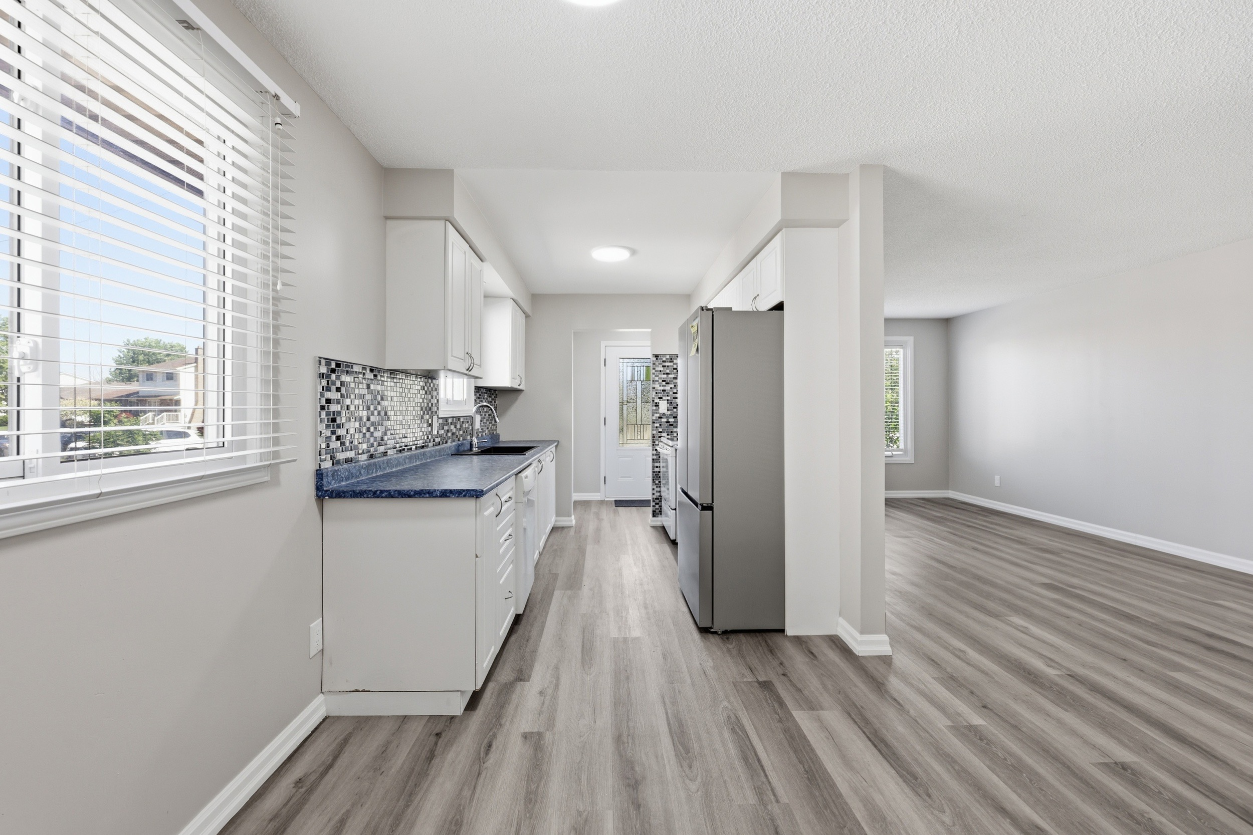 Galley kitchen with white cabinetry, mosaic backsplash, and stainless steel appliances