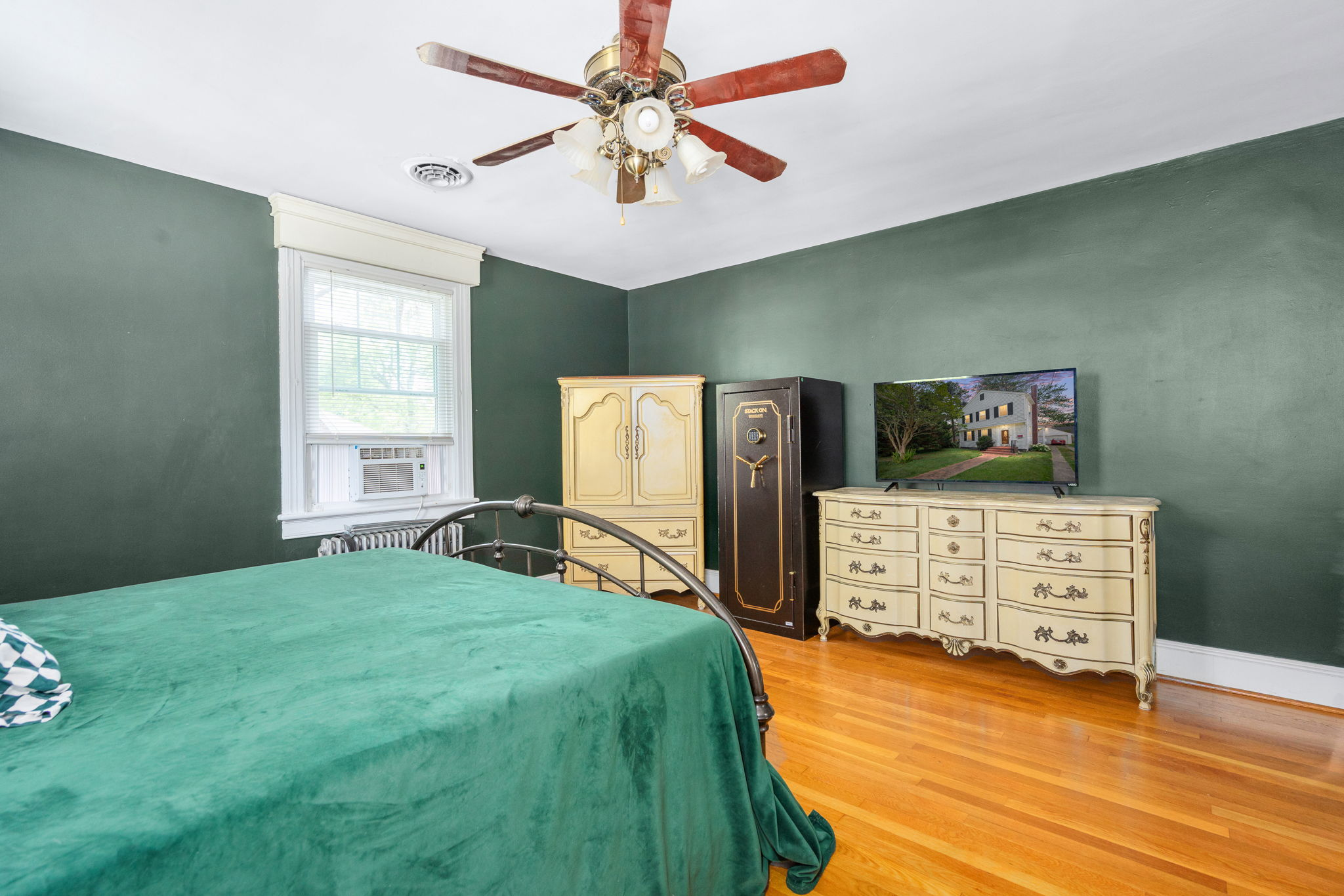 Primary bedroom with dark green walls and refinished hardwood floors