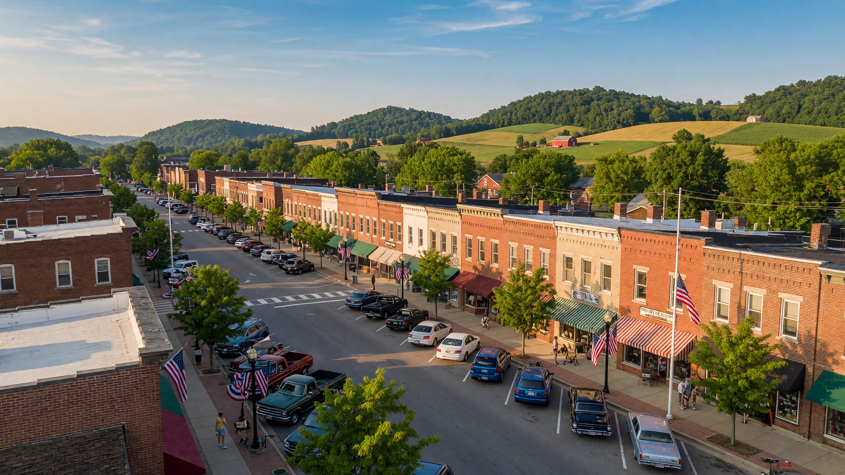 Aerial view of a charming small-town Main Street with brick storefronts, tree-lined sidewalks, and rolling hills