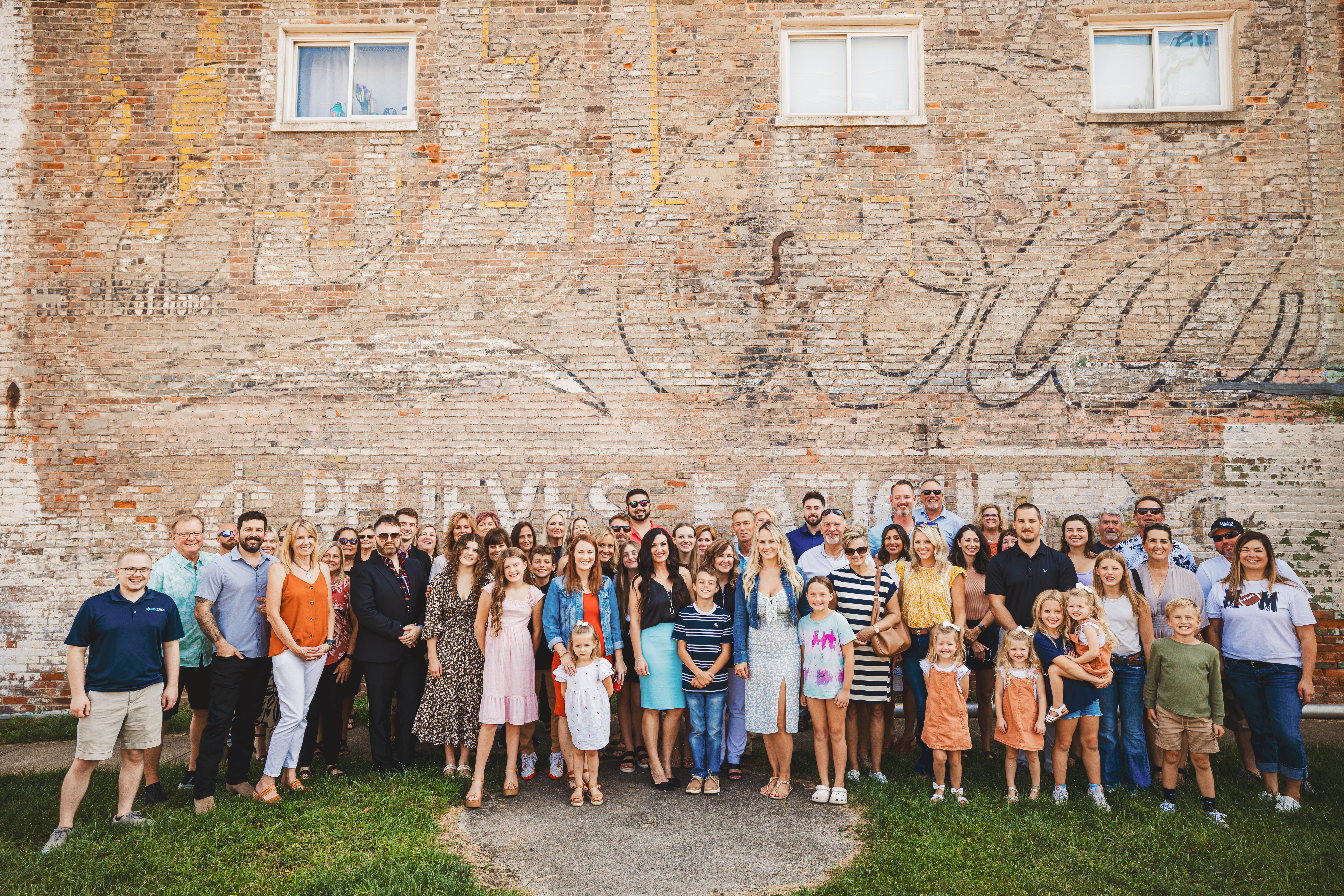 The Glasshouse Realty Wilmington office team — over 50 agents and staff posing together in front of a rustic brick building with a vintage Coca-Cola mural in downtown Wilmington, Ohio