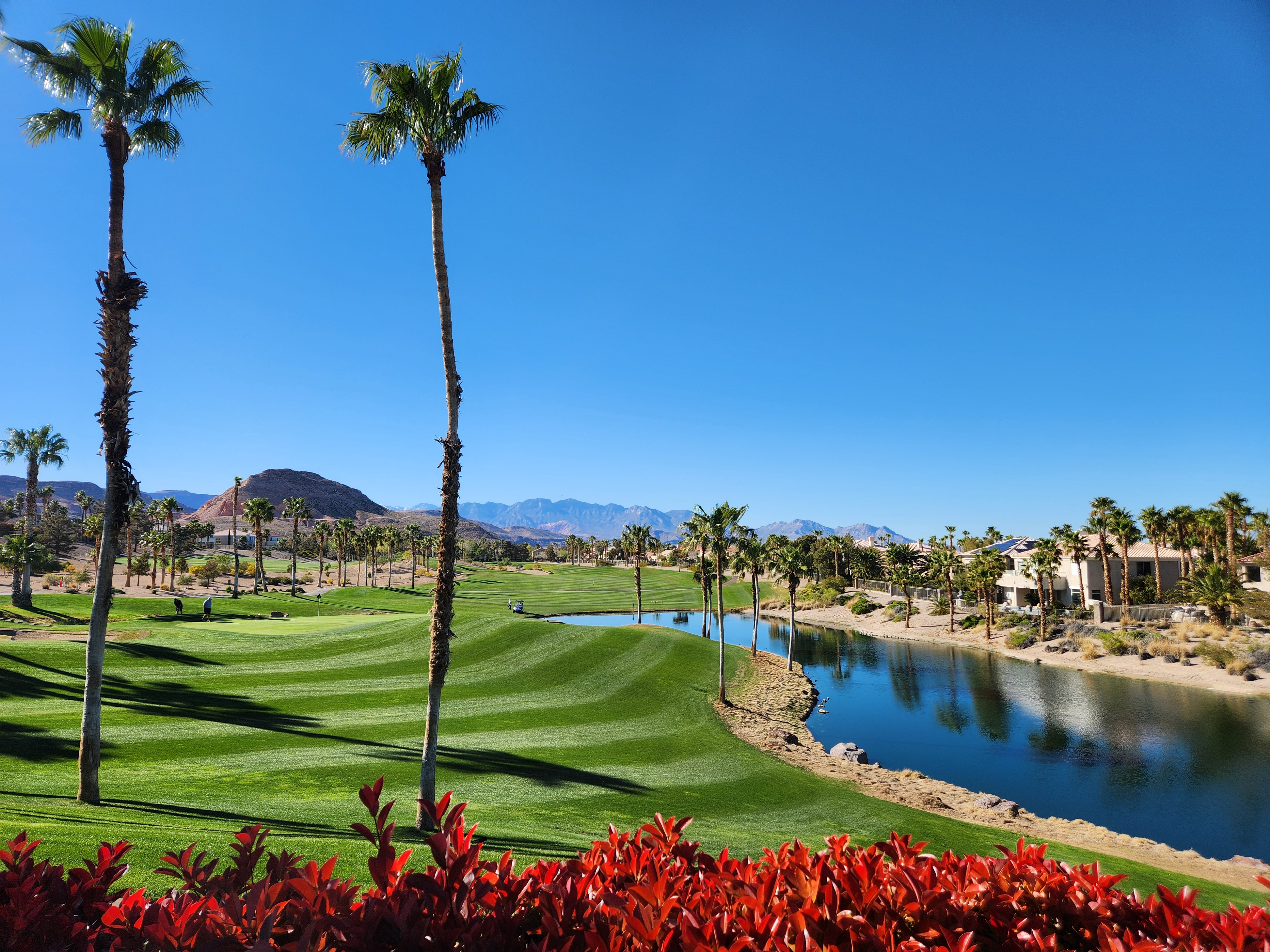Bright morning view over a manicured Rhodes Ranch golf fairway with a reflecting pond, palm trees, and desert mountains in the distance