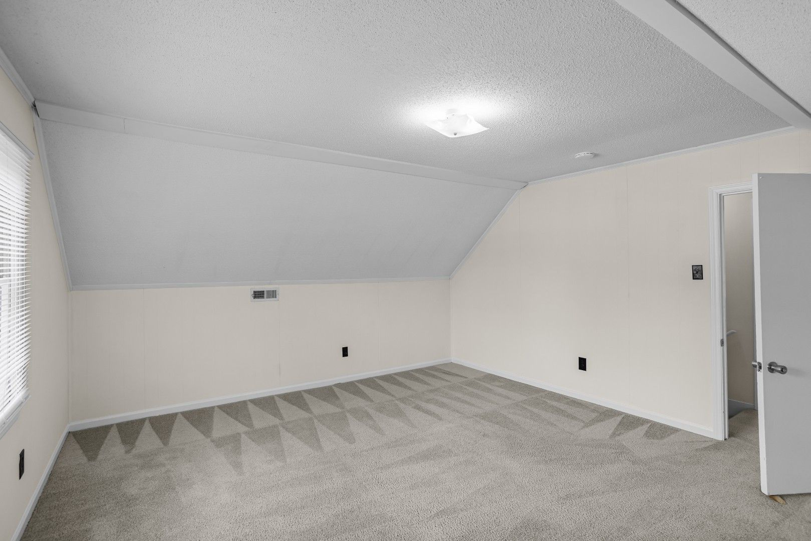 Upstairs bedroom with sloped ceilings, fresh carpet, and neutral finishes