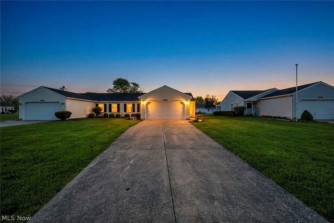 Twilight view of the front exterior with accent lighting illuminating the garage and entry