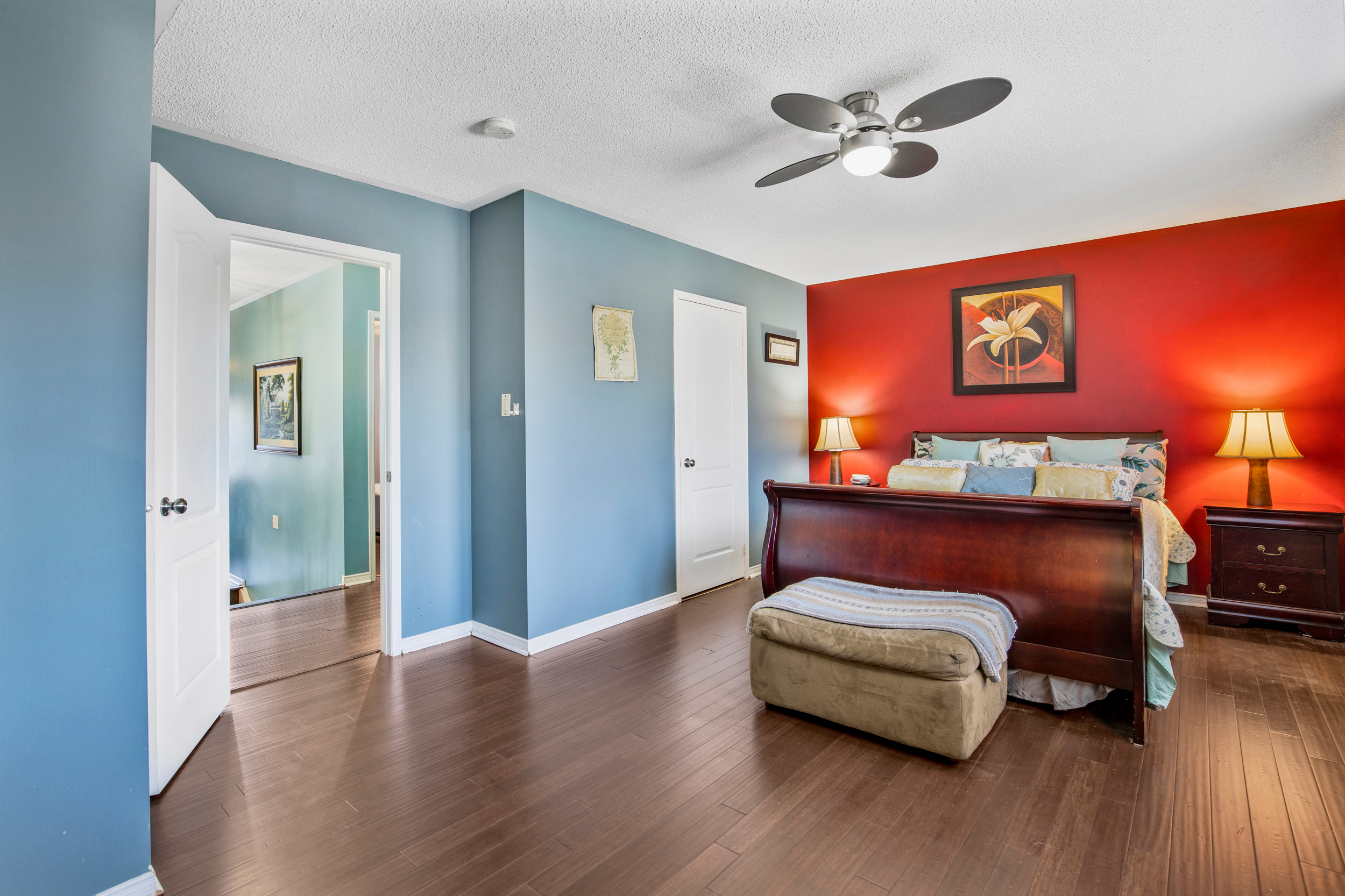 Primary bedroom with red accent wall and dark wood flooring