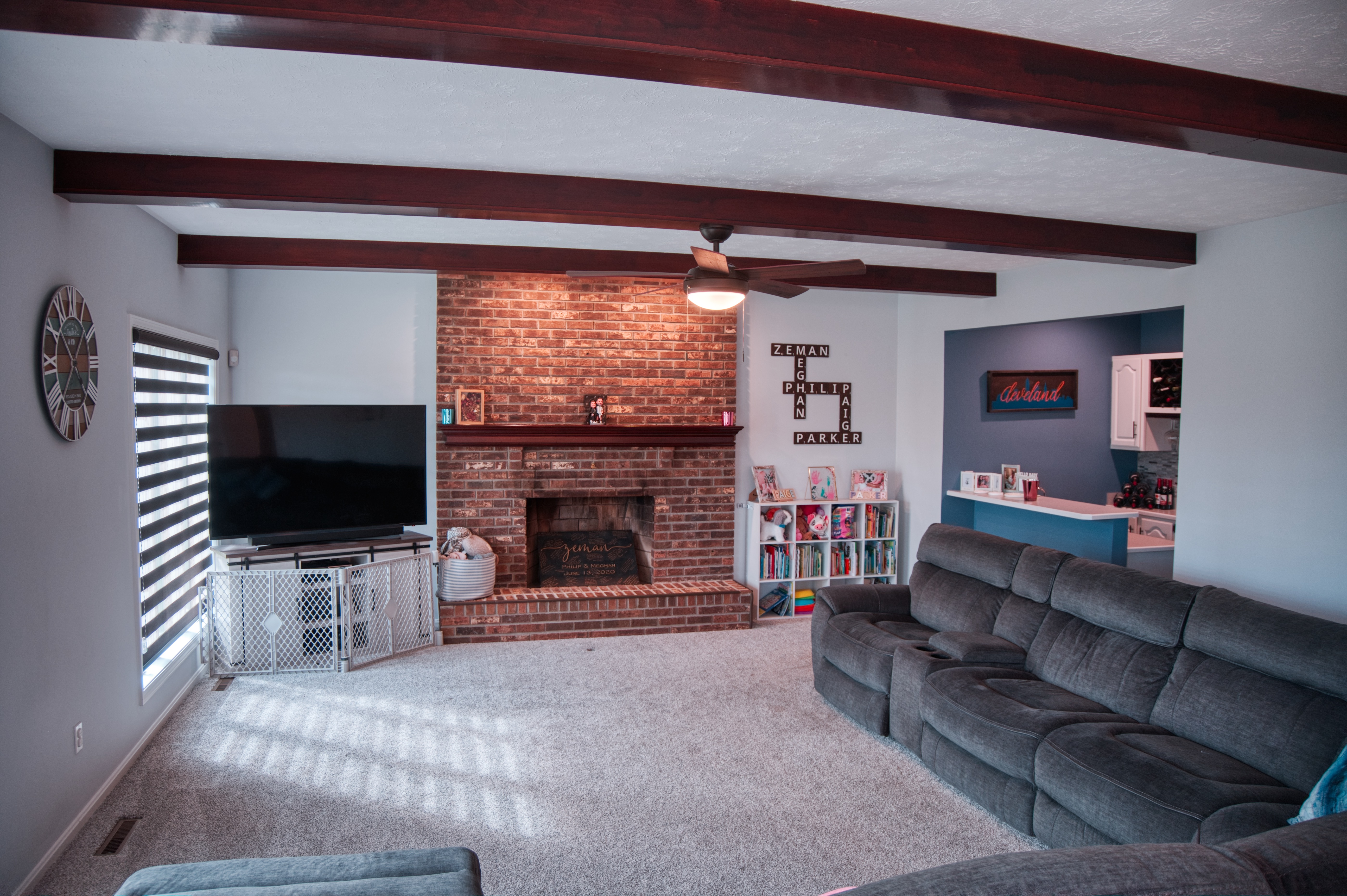 Living room with brick fireplace focal point, exposed wooden ceiling beams, and carpeted floor
