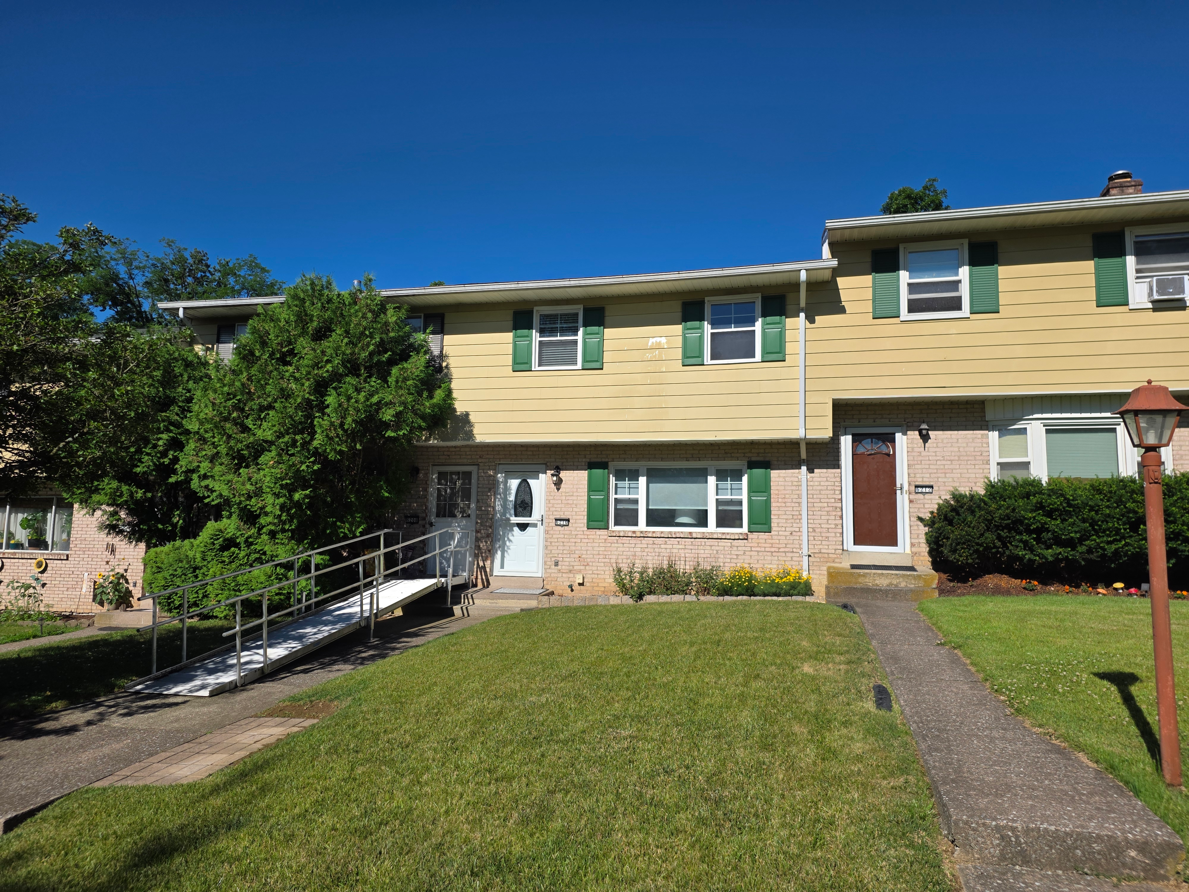 Multi-unit townhouse facade with beige vinyl siding, brick veneer, green shutters, and blue sky