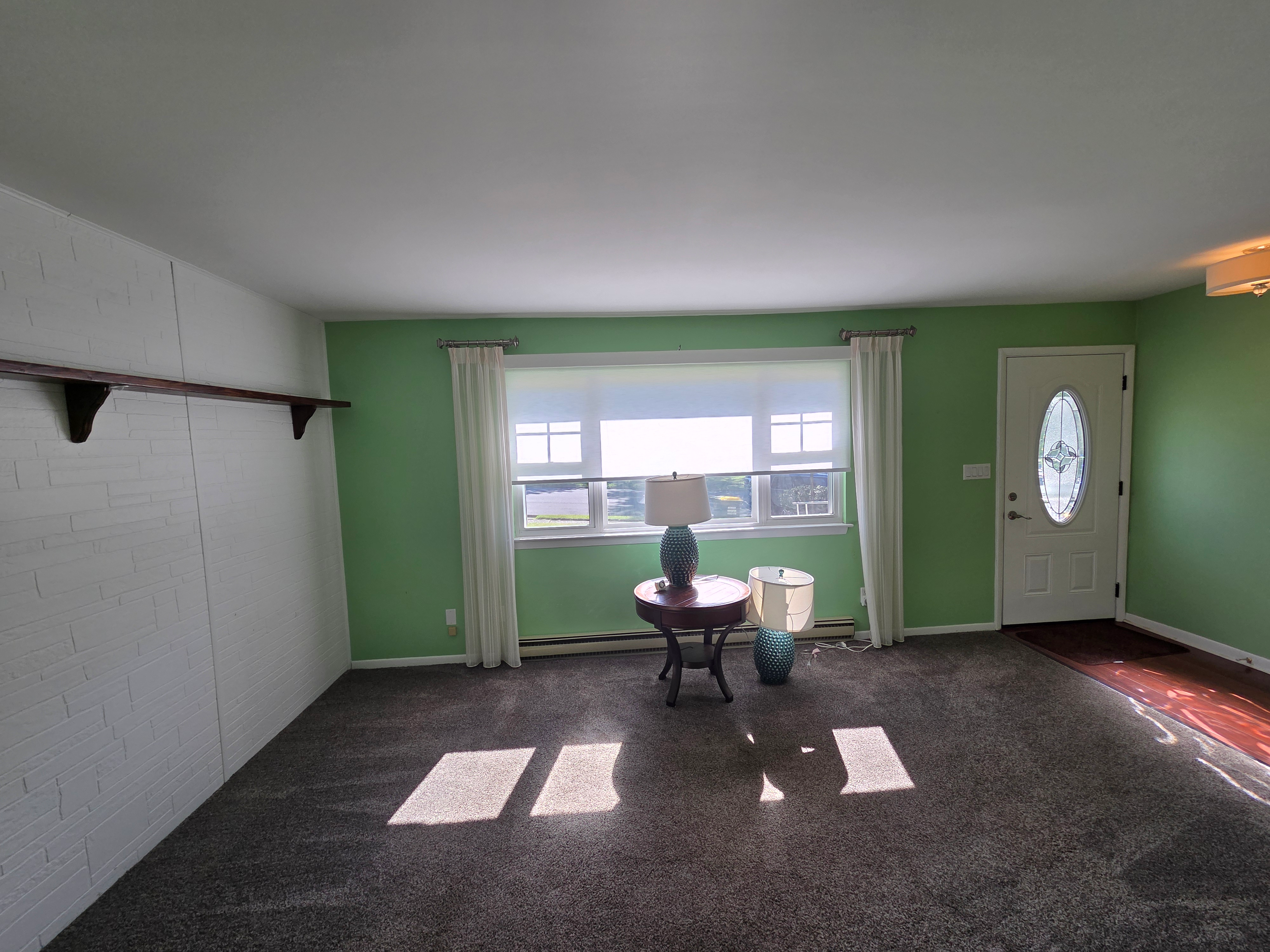 Living room facing front entry door with painted brick feature wall and natural daylight
