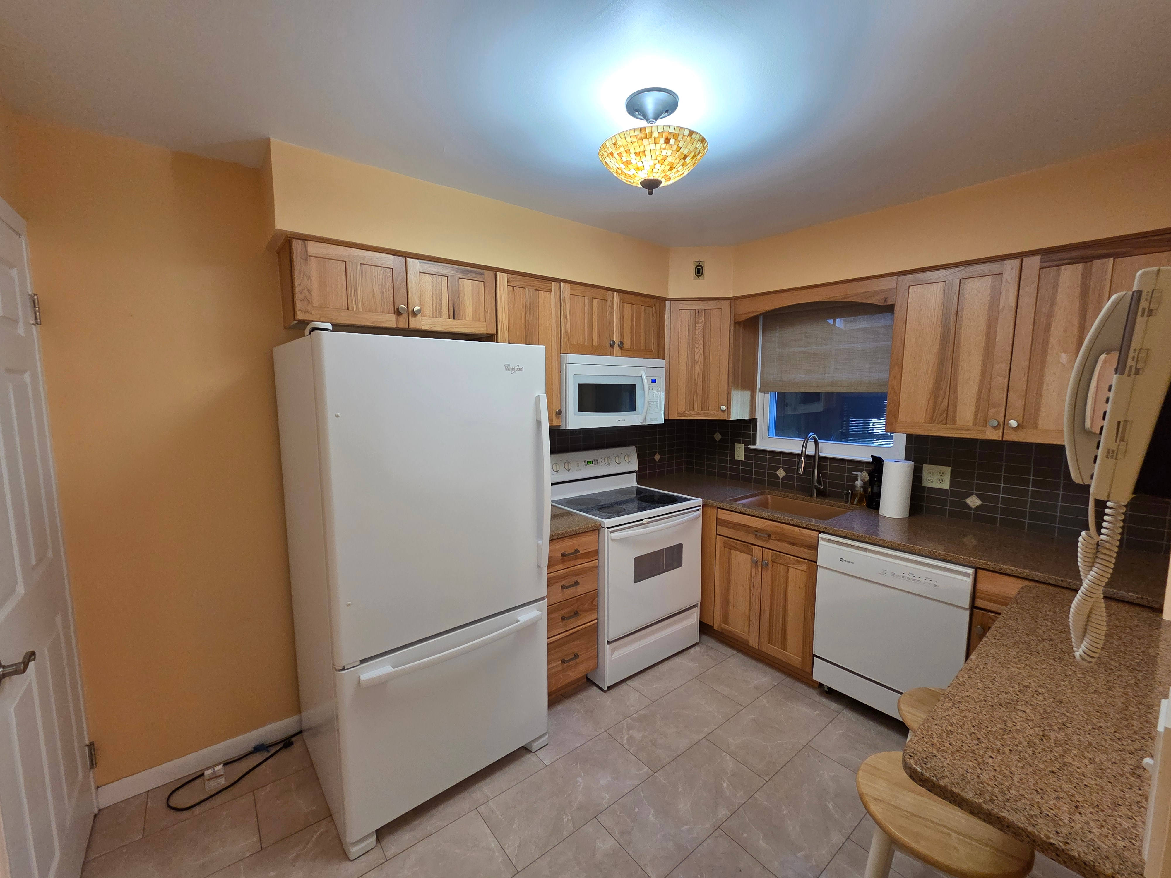 Kitchen showing honey oak cabinetry, granite countertops, tile backsplash with natural window light