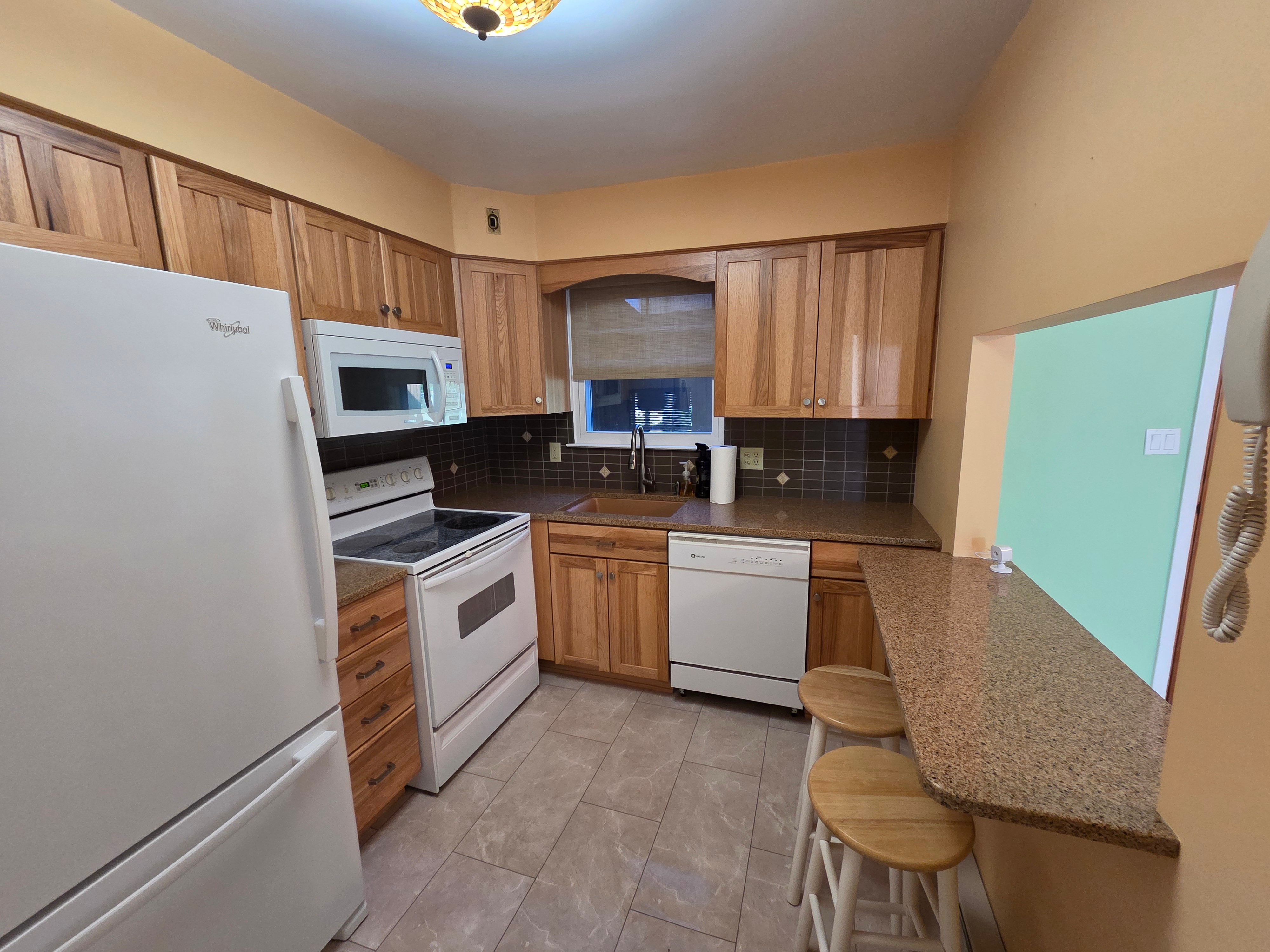 Eat-in kitchen with oak cabinetry, granite countertops, tiled backsplash, and white appliances at 6210 Glen Court
