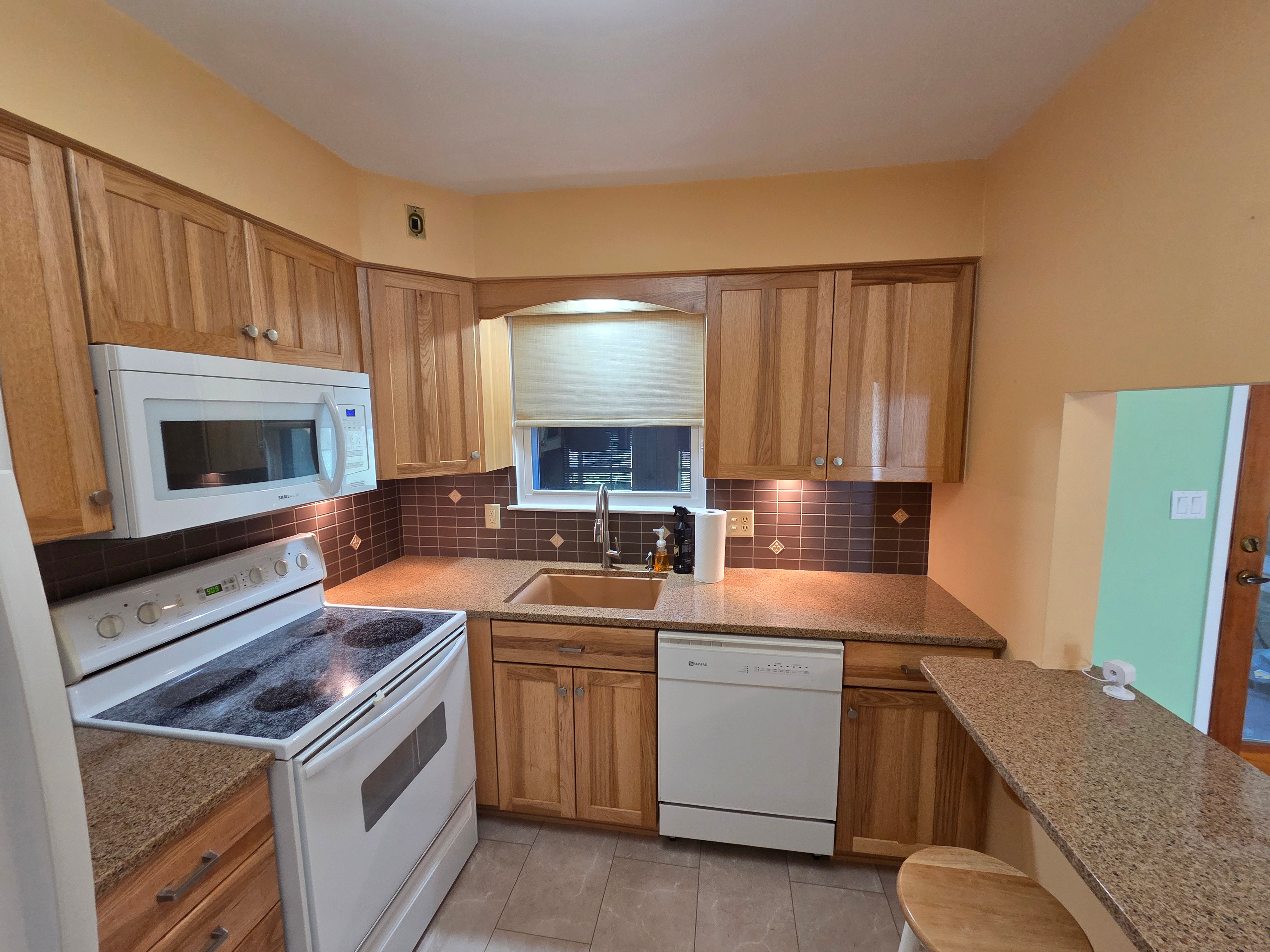 Kitchen sink area with oak cabinets, granite countertops, dark tiled backsplash, and under-cabinet lighting