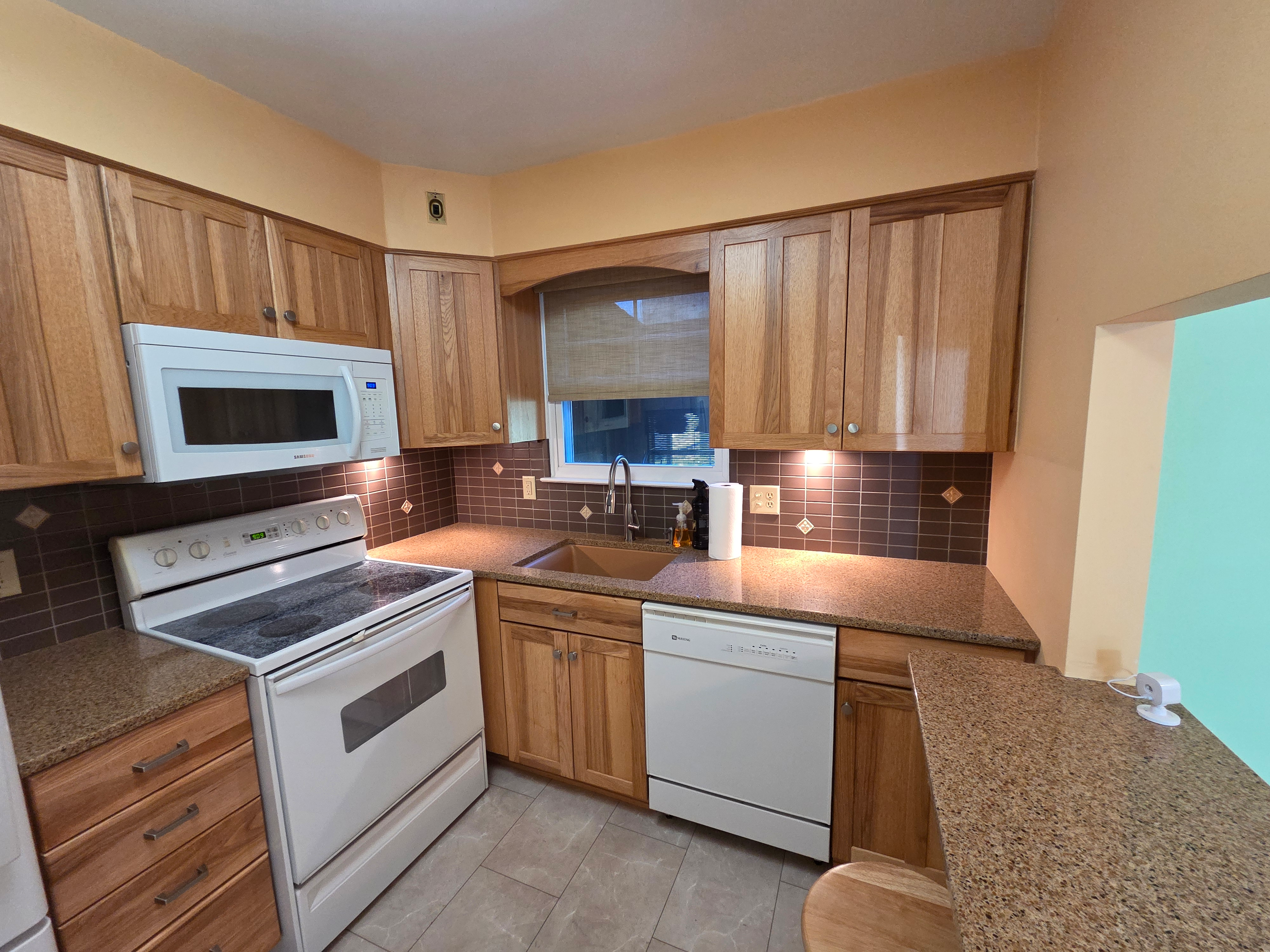 Kitchen with natural oak cabinetry, granite countertops, decorative tile backsplash, and white appliances