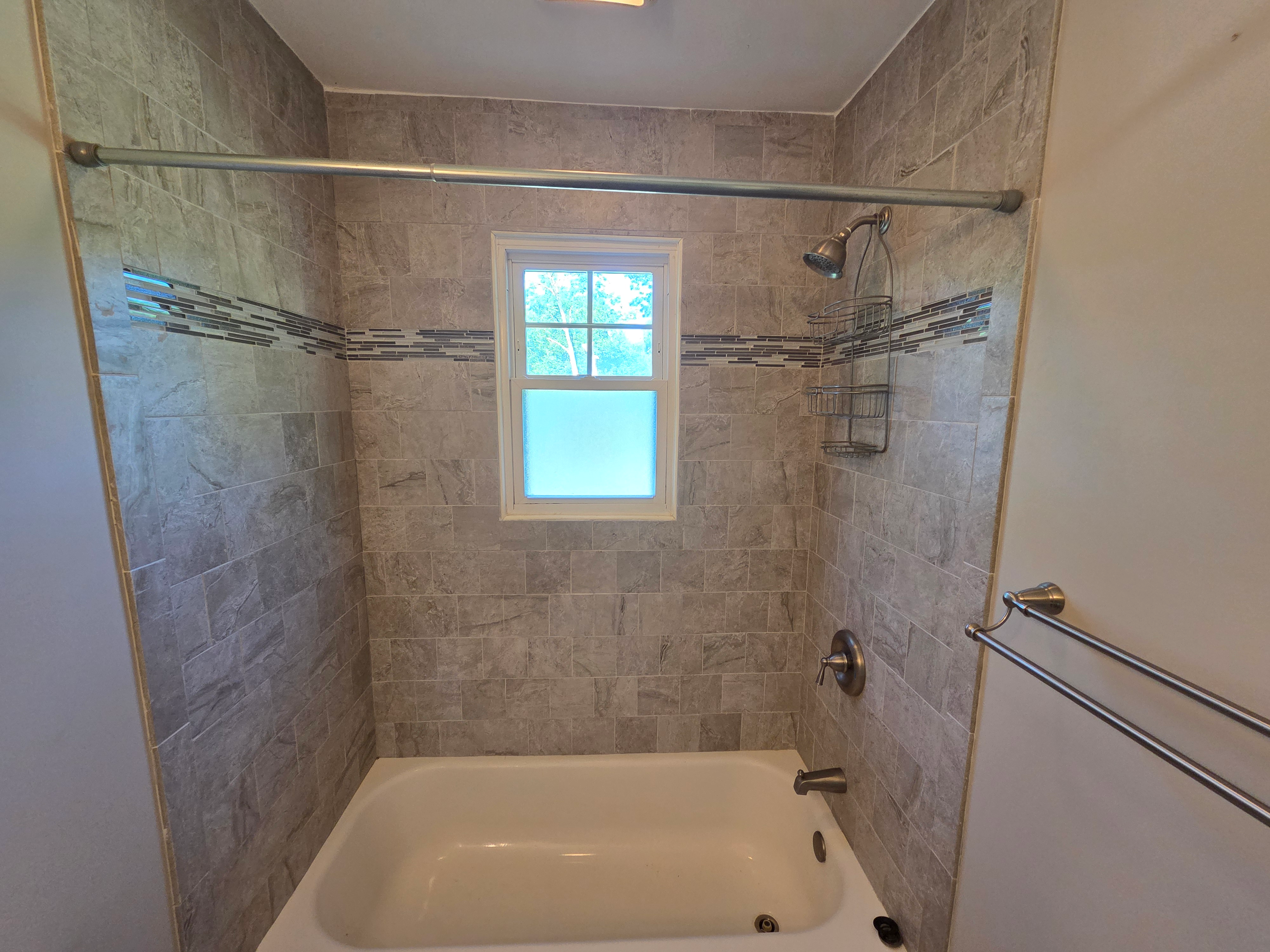 Remodeled full bathroom with modern neutral stone-look ceramic tiling and mosaic accent strip